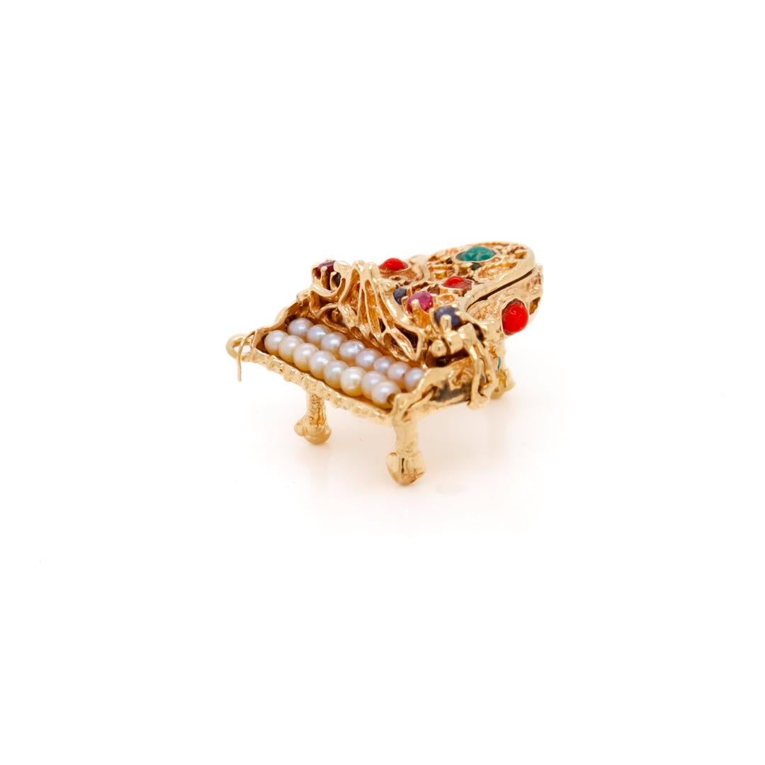 A fine vintage figural piano gold charm for a charm bracelet.

In 14k gold.

Set with pearls as piano keys, and decorated throughout with applied gold wirework.  

Bezel-set coral and turquoise cabochons, and prong set with tiny rubies and