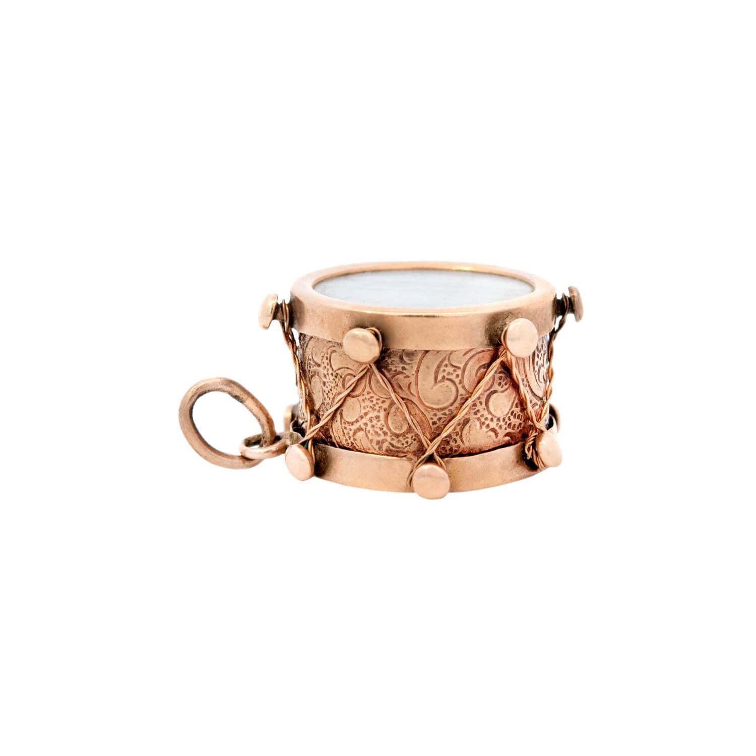 A beautiful Retro snare drum charm from the Retro (ca1950s) era! Crafted in 14k yellow gold, this piece resembles a snare drum. The shell of the drum features intricate raised details, and scrolling and foliage etchings. The batter head of the drum