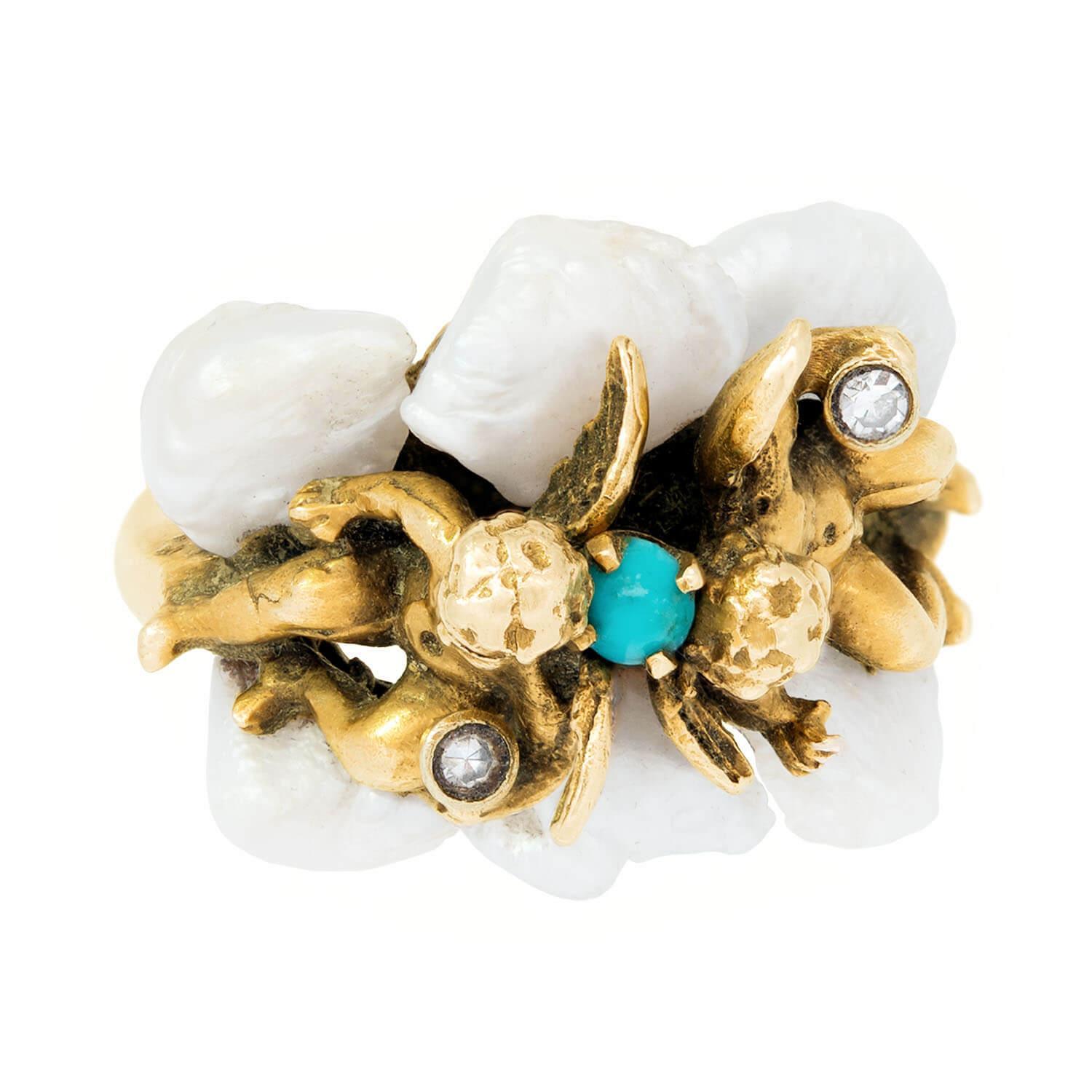 A unique and highly-detailed cherub ring from the Retro (ca1960s) era! Crafted in 14k yellow gold, this ring depicts two, three-dimensional winged cherubs sitting with their backs pressed against one another. A small turquoise cabochon is wedged