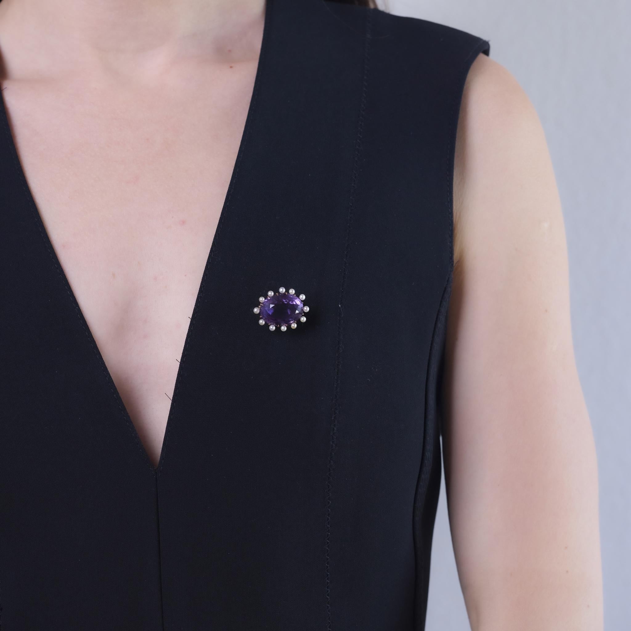 This Retro brooch from the 1940s is crafted in 14k rose gold and features a richly colored oval cut amethyst weighing approximately 15.60 carats. Surrounding the center are twelve cultured pearls, each measuring approximately 2.94mm, adding soft