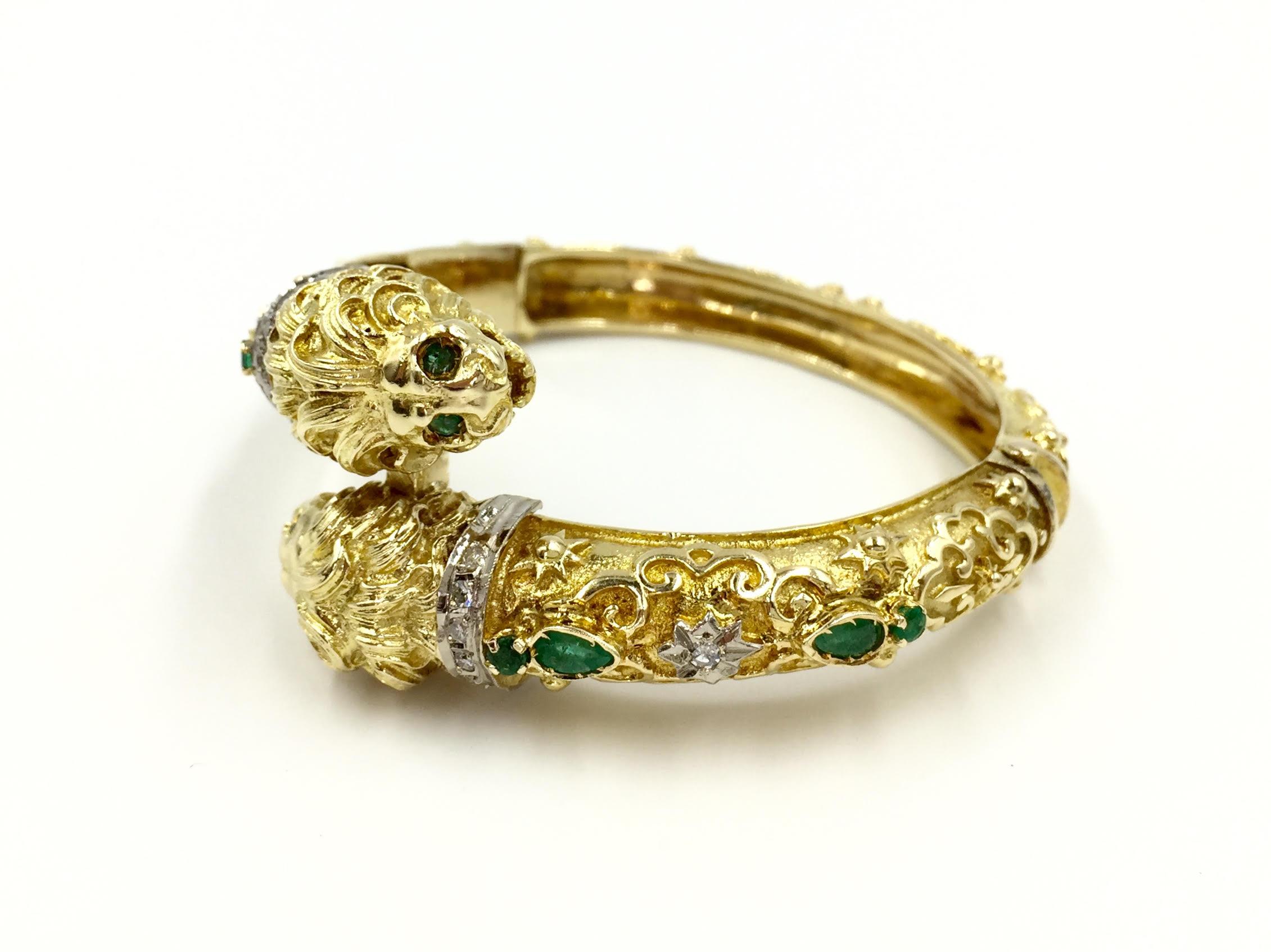 Circa 1960's. A one of a kind find. This unique handmade 18 karat yellow gold bypass style bangle has gorgeous detail and finish from every angle. Two lions heads are adored with emerald eyes and diamond collars. Snap closure with an easy to use