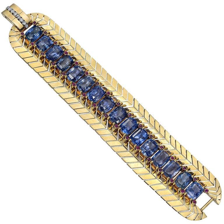 Retro wide link bracelet, centering a line of larger cushion-shaped ceylon sapphires flanked by smaller circular-cut bezel-set ruby accents and diamonds, in polished 14k yellow gold.

16 sapphires weighing ~100.00 total carats
34 rubies weighing