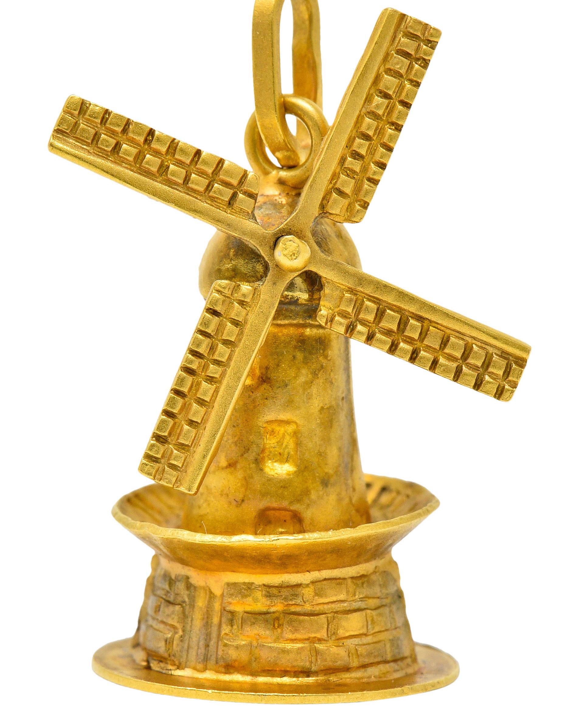 Substantially sized charm designed as a matte gold Dutch windmill

With a rotating propellers, deeply engraved with a checkerboard motif

Smooth tower with a base as highly rendered brick

Completed by jump ring bale

Circa: 1950s

Stamped K18 for