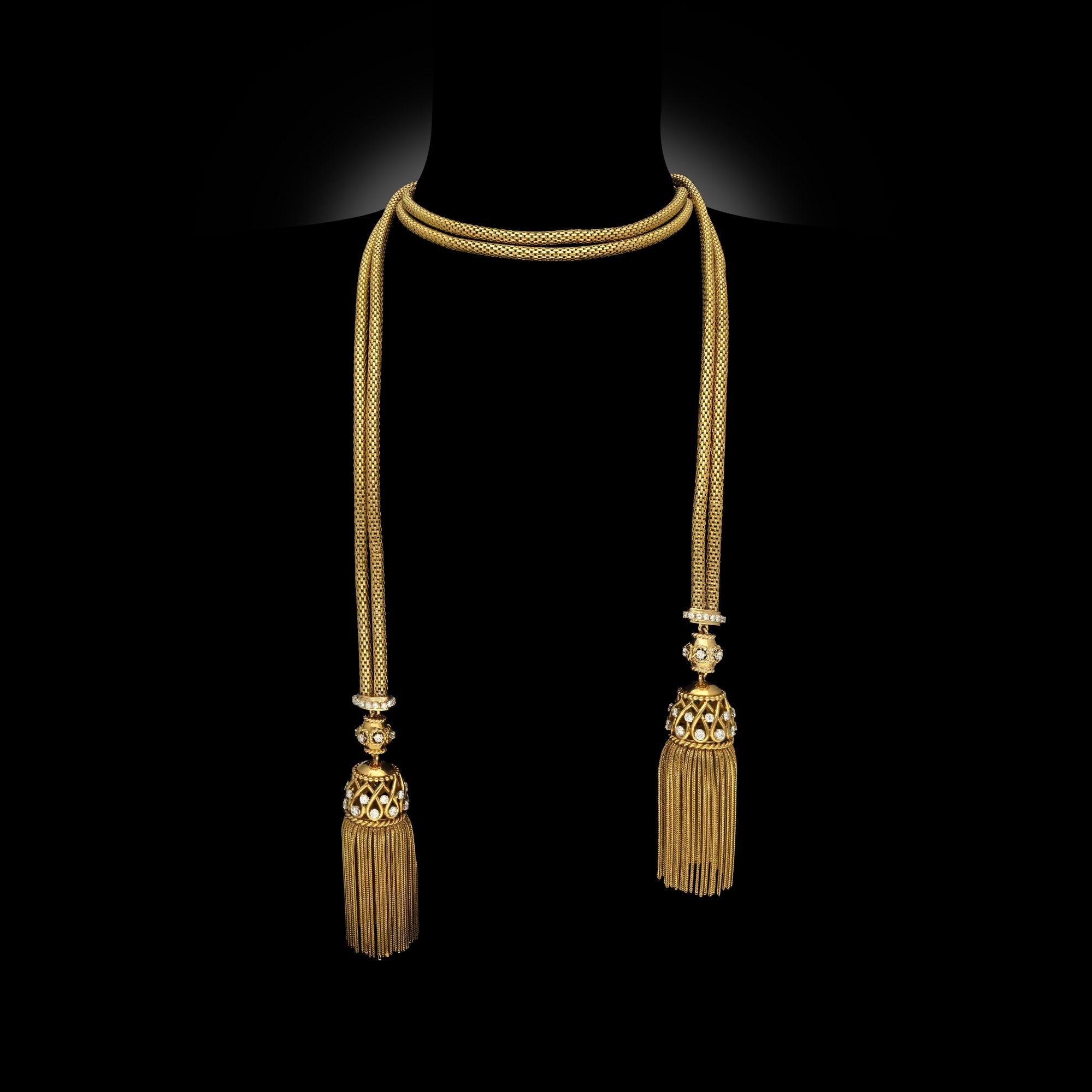 Collier sautoir en or jaune 18 ct et diamants à deux pompons, vers 1950. Le collier ouvert est composé de deux longueurs de chaînes à mailles arrondies, reliées par un bouchon serti de diamants à chaque extrémité, d'où pend un pompon à franges