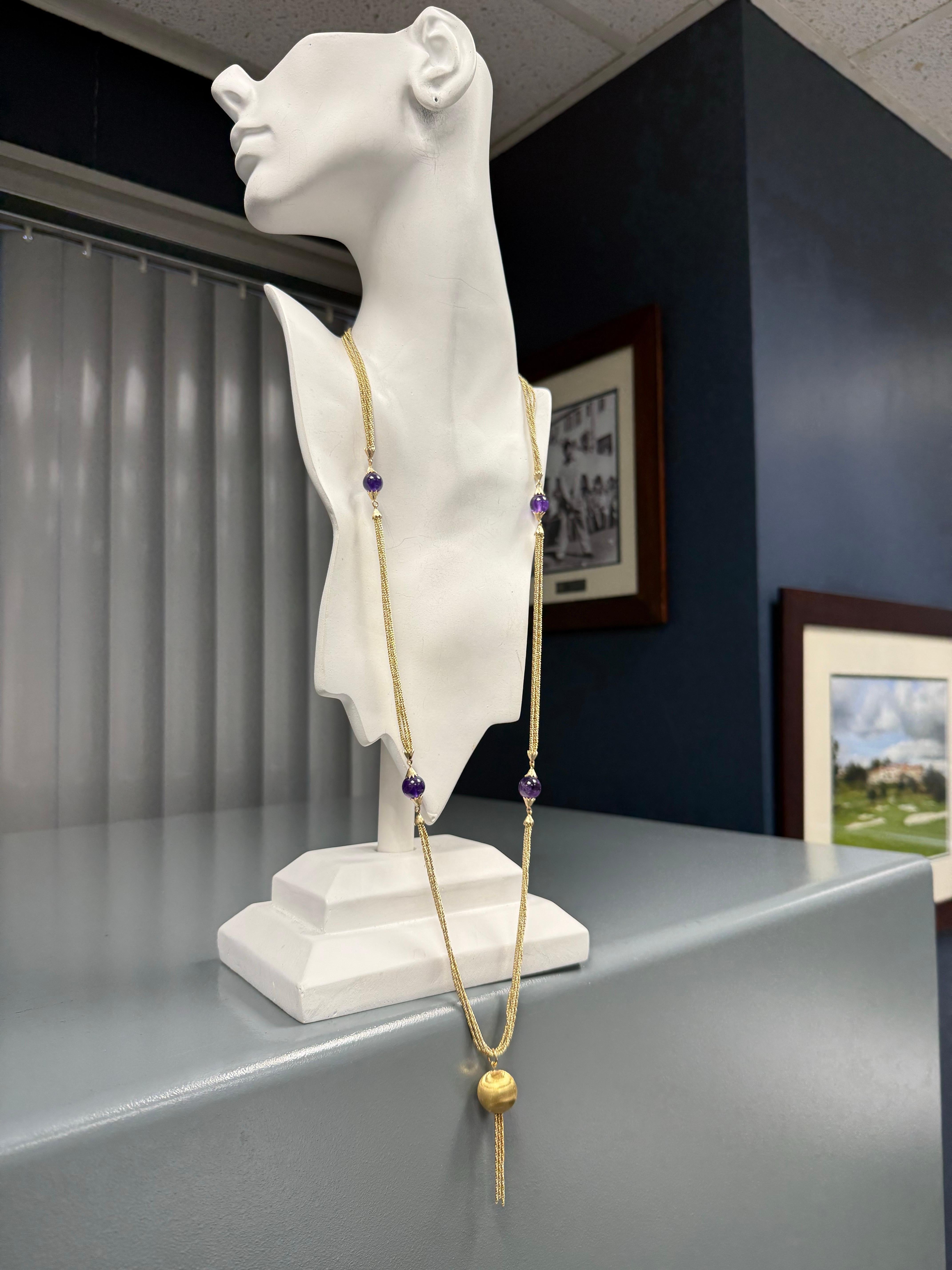 This retro 18K yellow gold five-strand opera-length statement necklace measures an elegant 34 inches in length and is accented with four rich purple amethyst beads measuring approximate 12 mm in diameter each. Suspended at the lower section is a