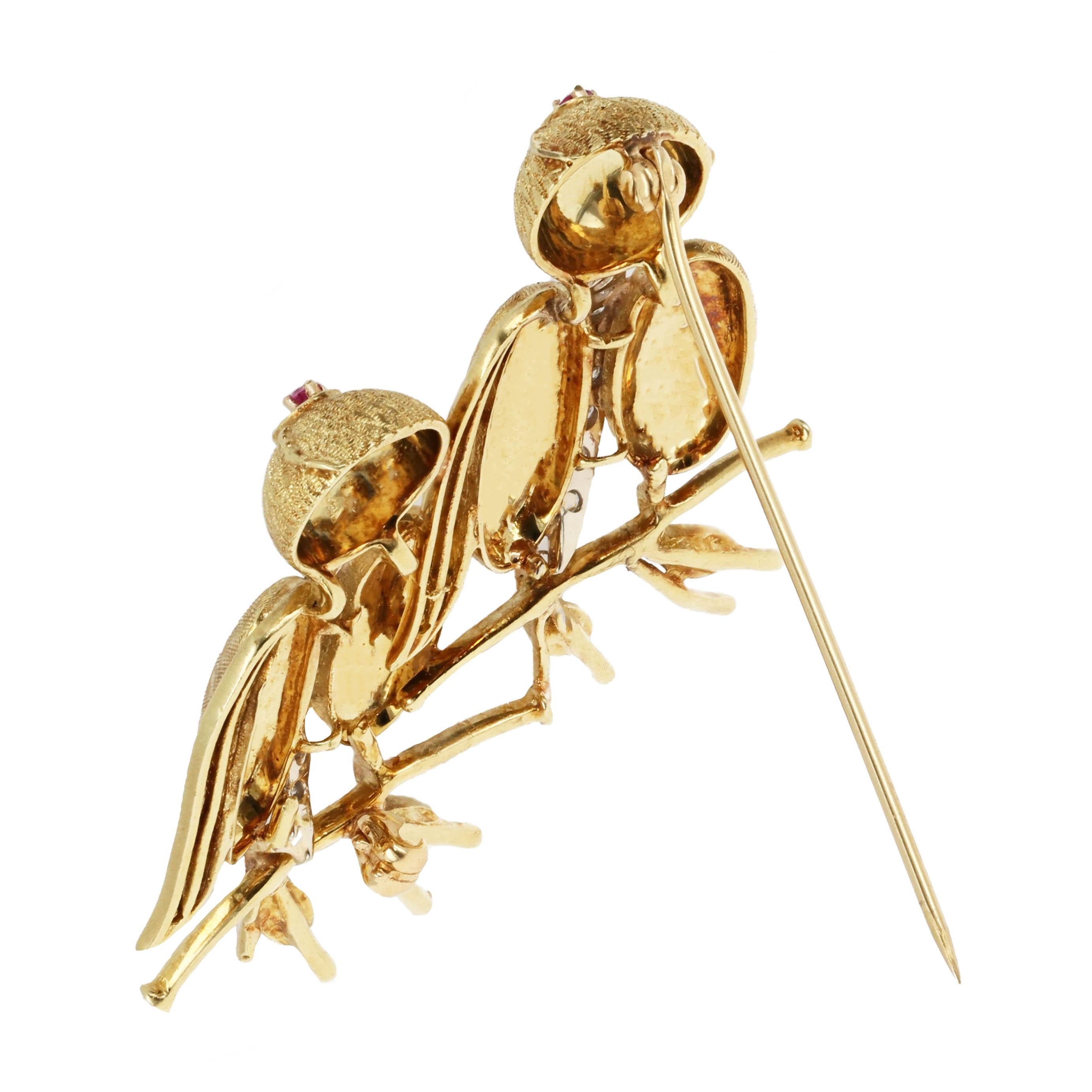 This retro 18 karat gold bird brooch showcases two whimsical birds perched gracefully on a branch, crafted in rich 18K yellow and white gold. The bodies of the birds are beautifully textured with alternating finishes, while a vertical strip of white