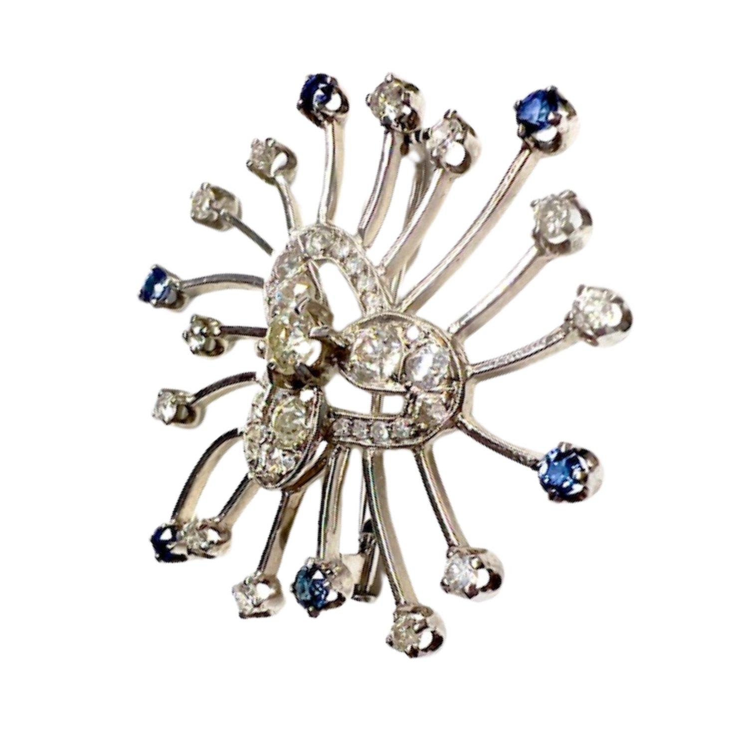 This retro-style brooch from the 1940-1945 period is crafted in 18K white gold and features antique-cut Diamonds and Ceylon Sapphires. 
It has a weight of 14.72 grams and measures 4.5 cm in length and 4.5 cm in width. 
The Diamonds total 3.09 carats