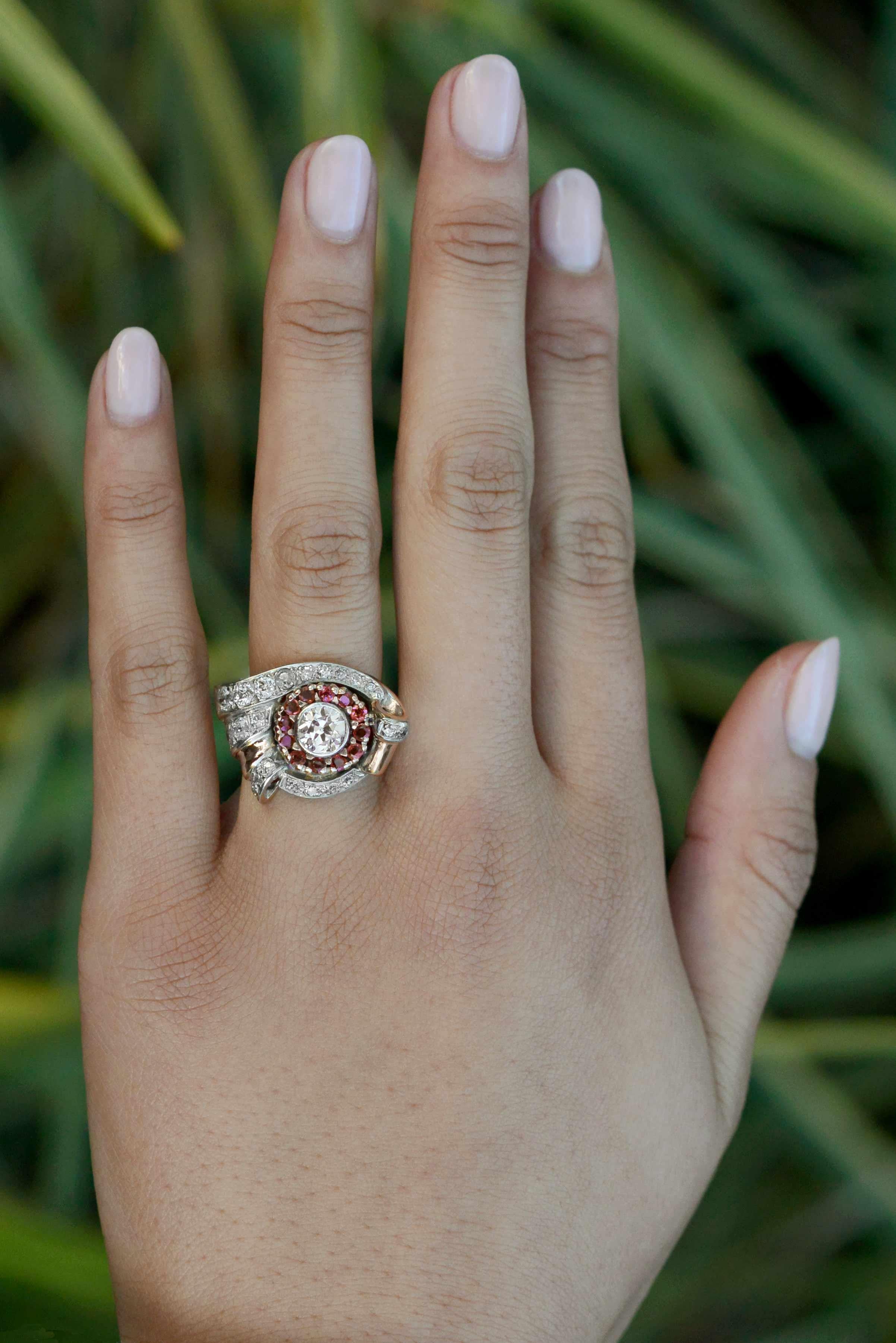 Make a Retro-lover's dream come true with this spectacular statement ring. Centered by a near carat, scintillatingly brilliant diamond nestled in a bezel setting. Bordering that is a glamorous halo of rubies accented by swirling, diamond-studded