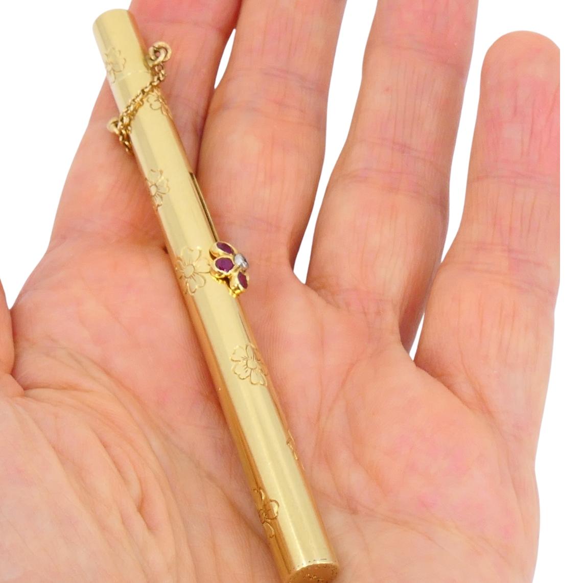 An elegant Van Cleef & Arpels retractable makeup brush. Crafted in 14k yellow gold, this luxurious accessory features exquisite floral engravings and a delicate ruby flower detail at the center. The retractable design reveals a fine brush that can