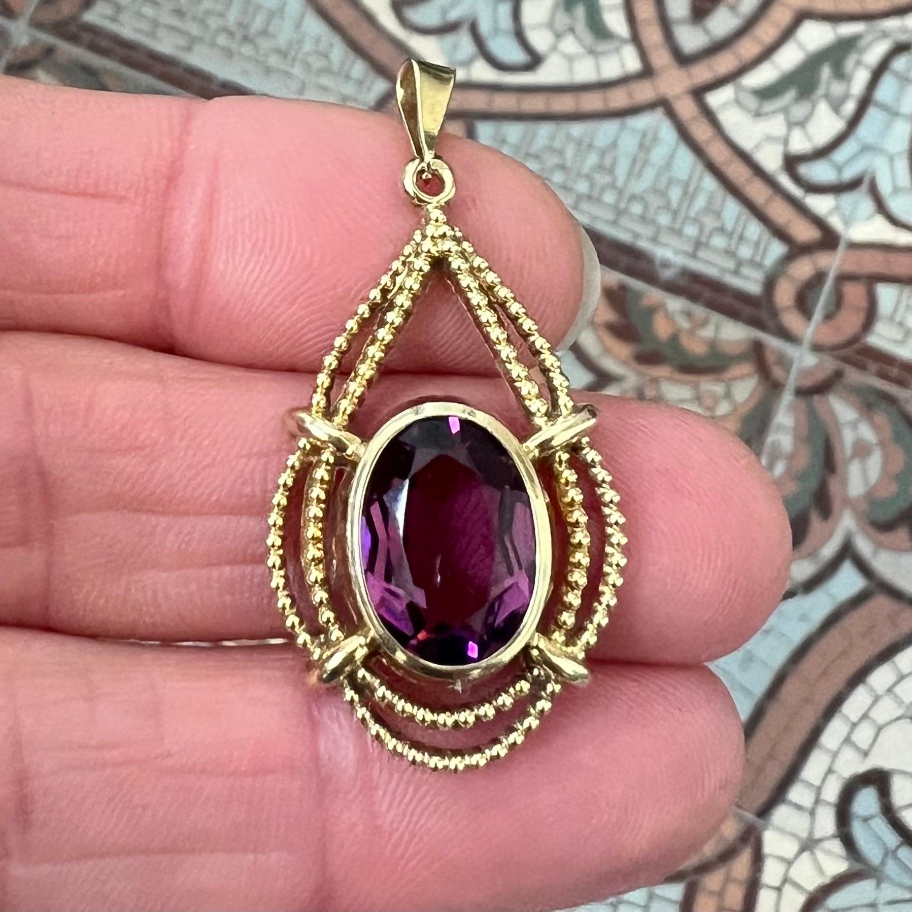 This elegant vintage pendant from the 1950's–1960's features a vibrant faceted amethyst set in a 14 karat gold frame. The amethyst, an oval-cut stone with rich purple hues, is securely held by four prominent prongs and encased in a finely detailed