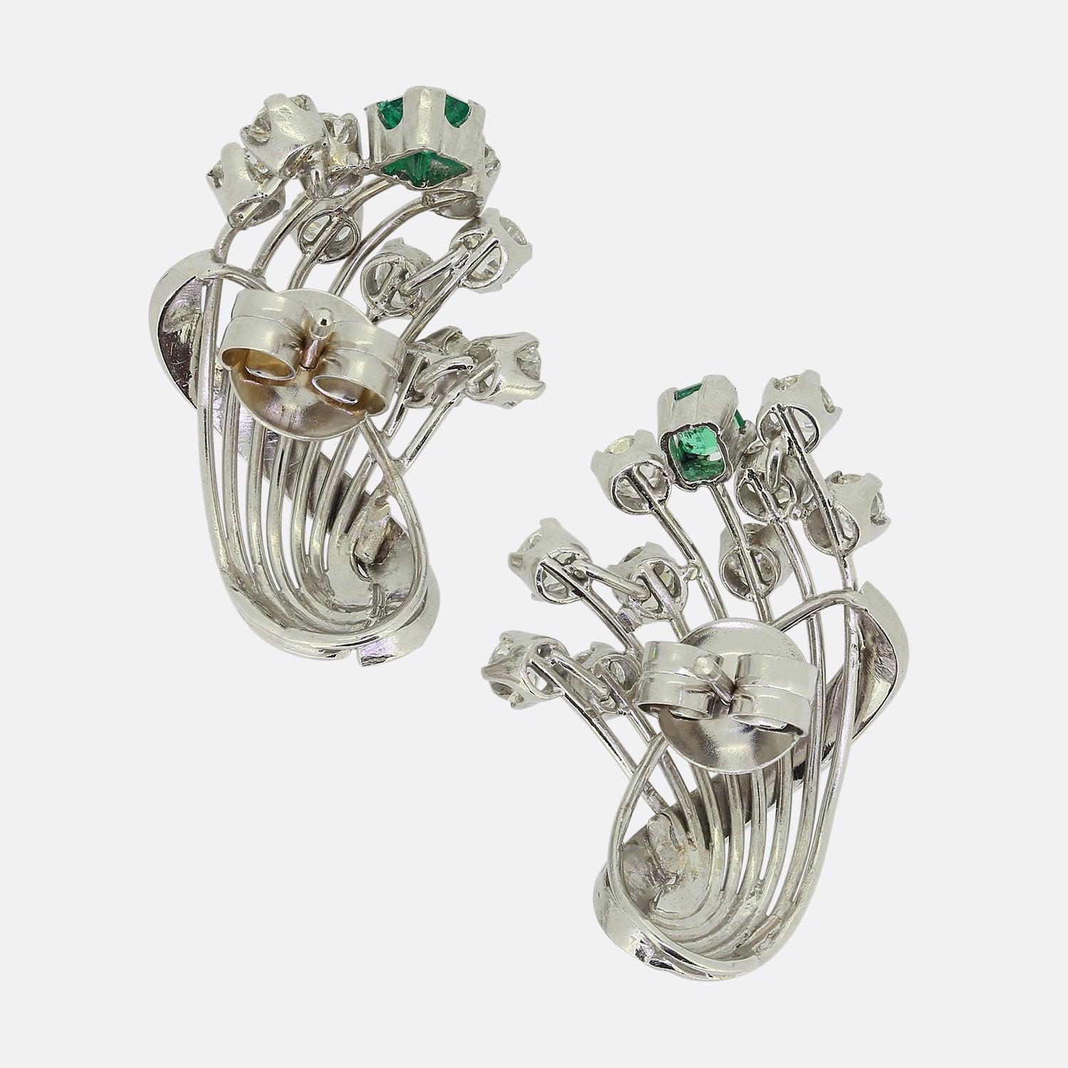 Here we have a fabulous pair of retro emerald and diamond earrings. Both open frames showcase a cluster of round faceted old cut diamonds with a single natural emerald for company; each of which is claw set atop an individual platinum stem. A ribbon