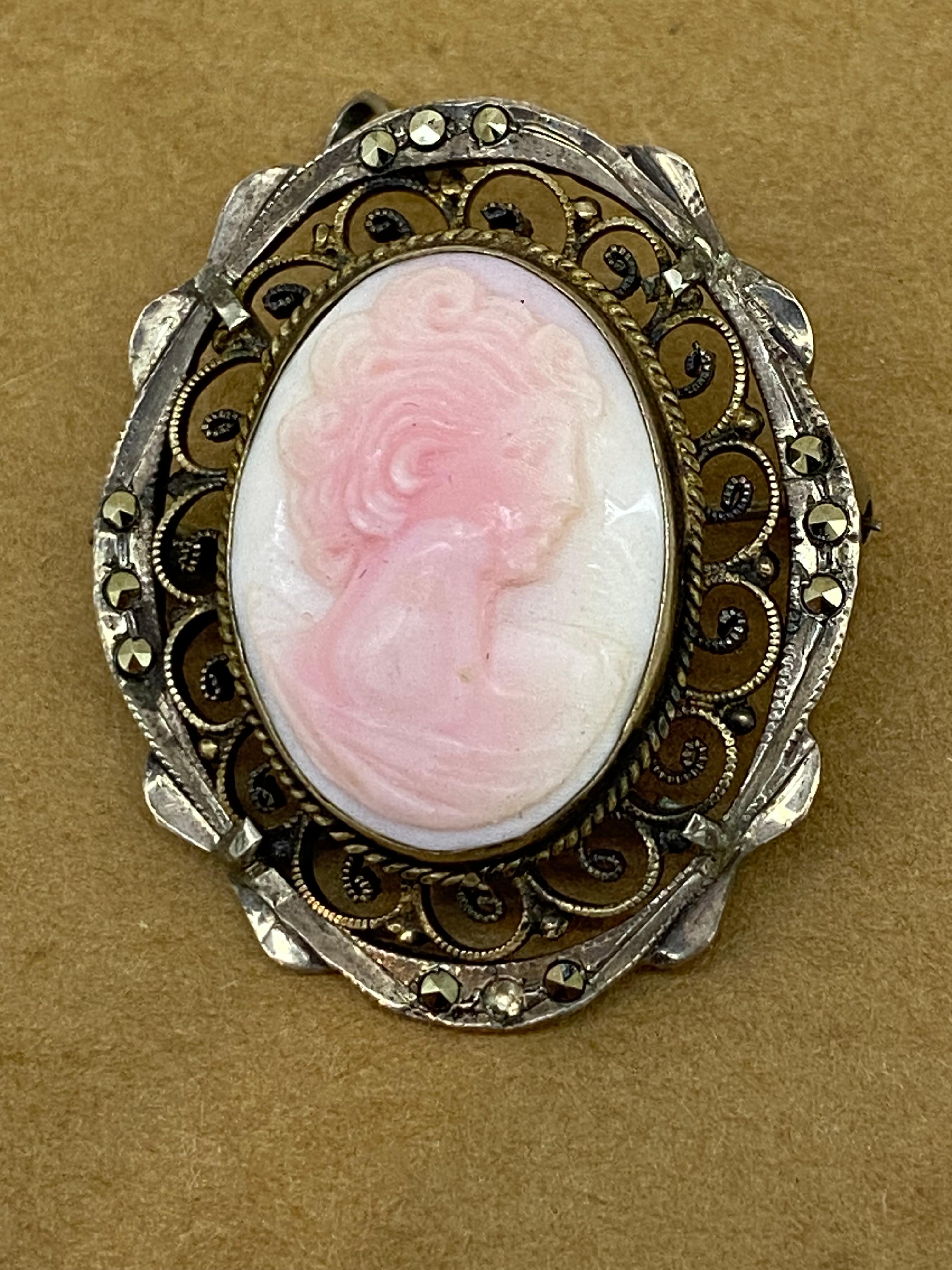 This Vintage Finely Carved Pinkish White Coral Brooch 

is depicting a profile of a young lady, 

incredibly detailed, 

within a 925 Sterling Silver finely detailed decorative border,

adorned with marcasites 

 

It has a pin & a bail - provision