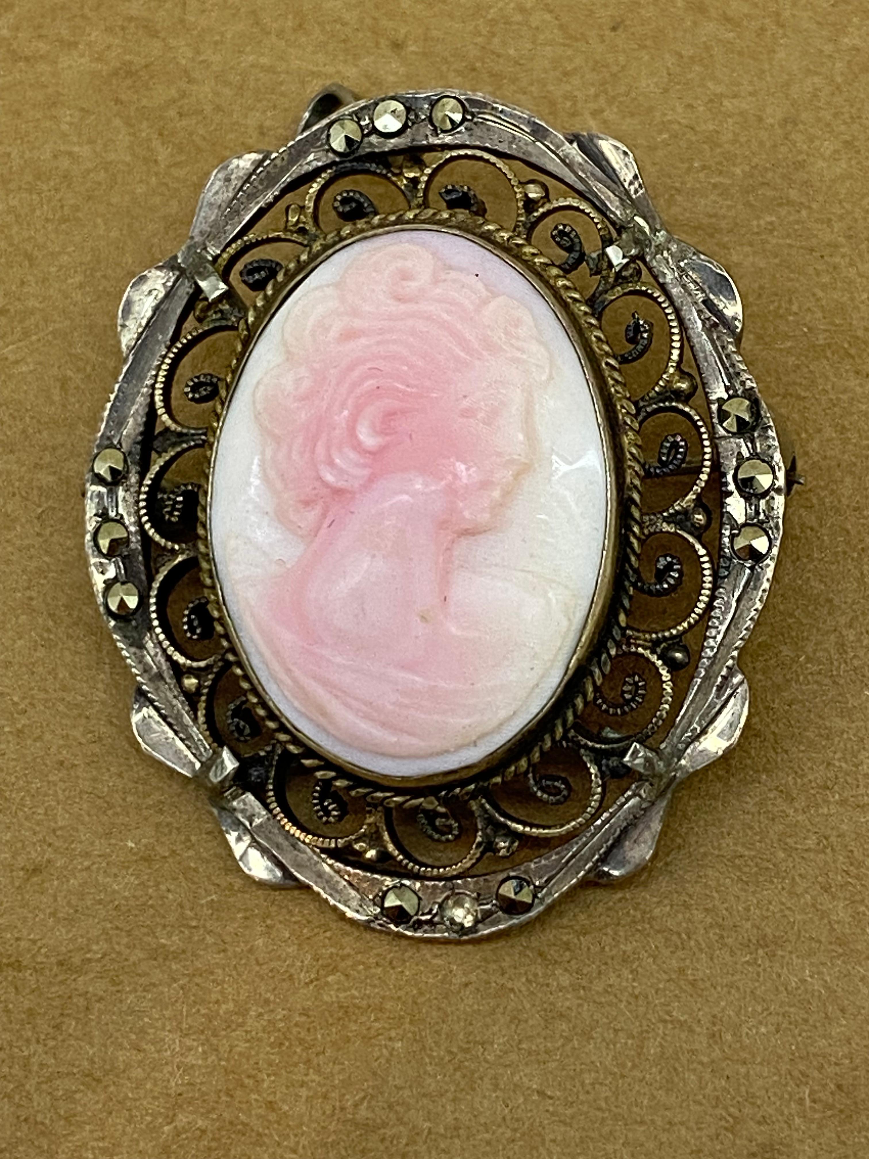 Diese Vintage fein geschnitzt Pinkish White Coral Brosche 

stellt das Profil einer jungen Frau dar, 

unglaublich detailliert, 

in einer fein gearbeiteten Zierleiste aus 925er Sterlingsilber,

geschmückt mit Markasiten 

 

Es hat einen Stift &