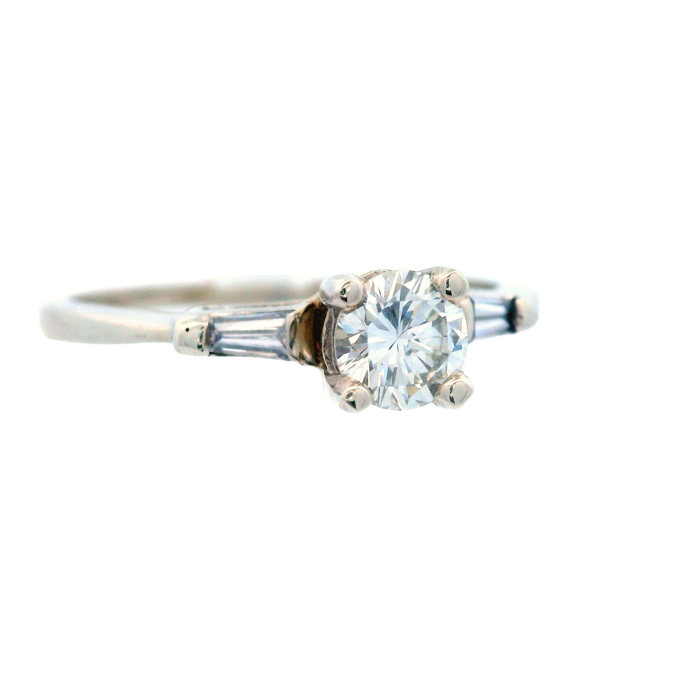 Questo delizioso anello è stato realizzato negli anni '60 con oro bianco a 14 carati e diamanti a taglio baguette e rotondo. Si tratta di un tradizionale anello con diamante a tre pietre con un tocco divertente e moderno dato dalle spalle di