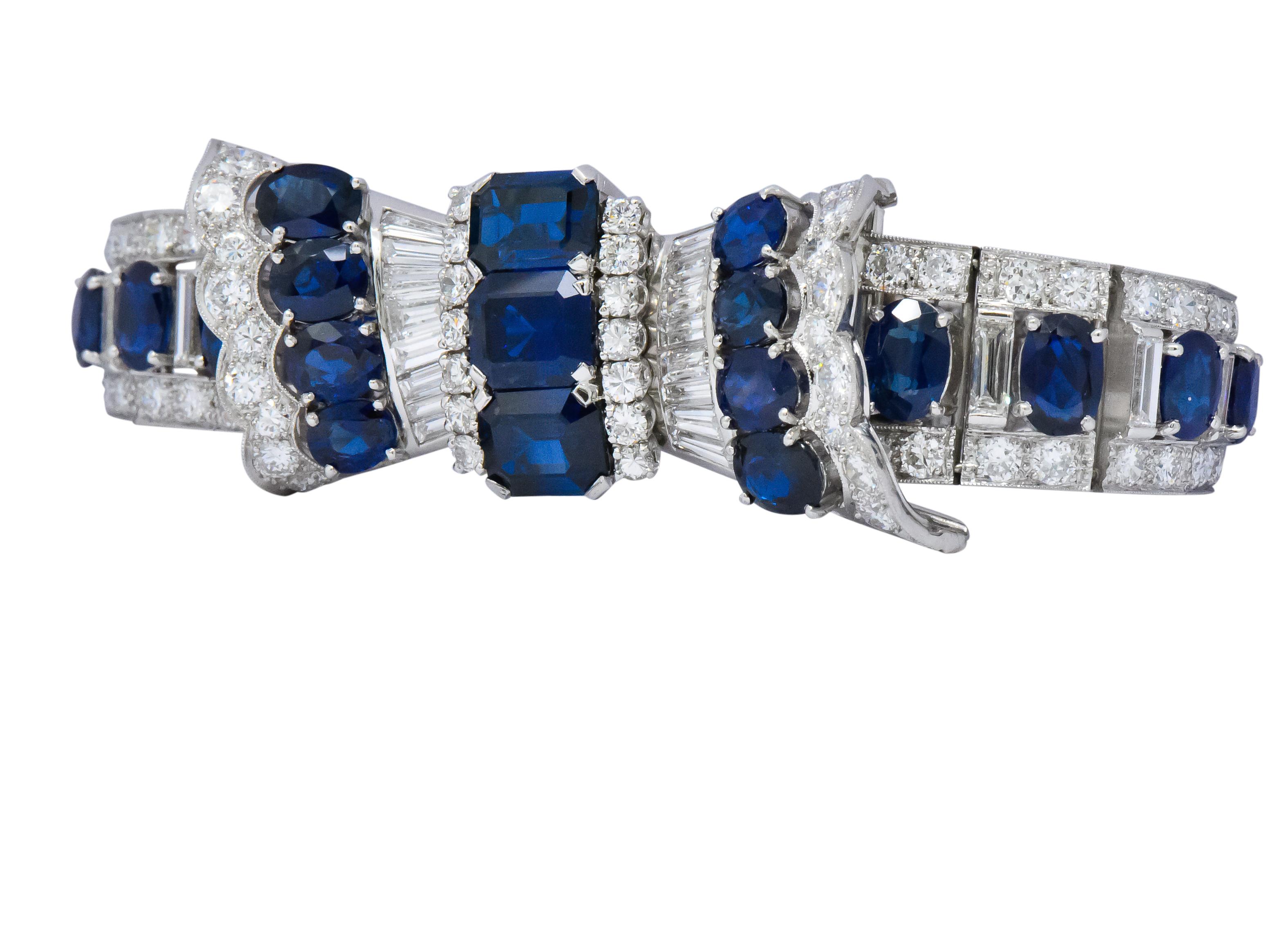 Bracelet is comprised of graduated square links with a stylized bow central station accented by milgrain and scalloped edges

Set throughout by emerald cut, round cut, and oval cut sapphire; transparent and an incredibly well-matched medium-dark