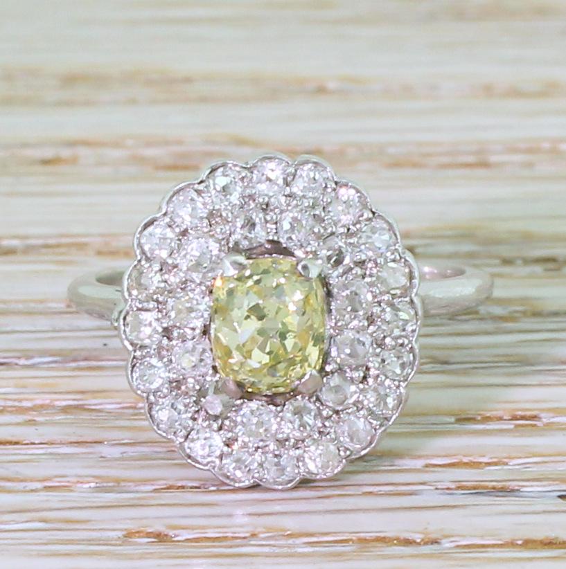 A vintage diamond cluster ring that displays unbelievable sparkle. The oval shape old mine cut diamond in the centre displays a strong, distinctive fancy yellow. A double halo of thirty-two white and bright old mine cut diamonds are pavé-set in the