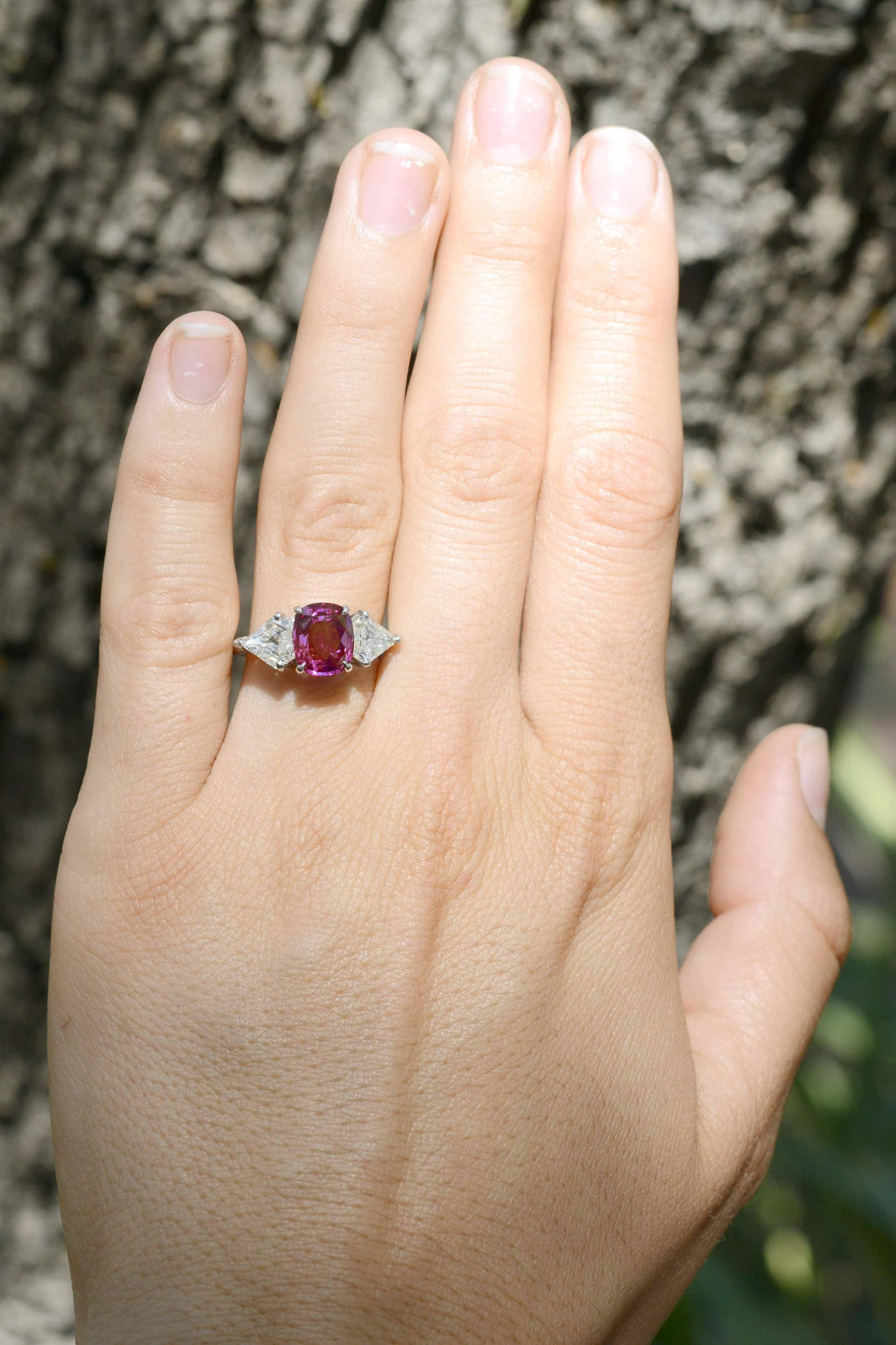 A vivacious, vintage pink sapphire and diamond engagement ring. Centered by a GIA certified 2.14 carat natural sapphire of a juicy, bubble gum pink cushion cut gemstone. Contrasted by a pair of rare, ravishing kite shape diamonds weighing a combined