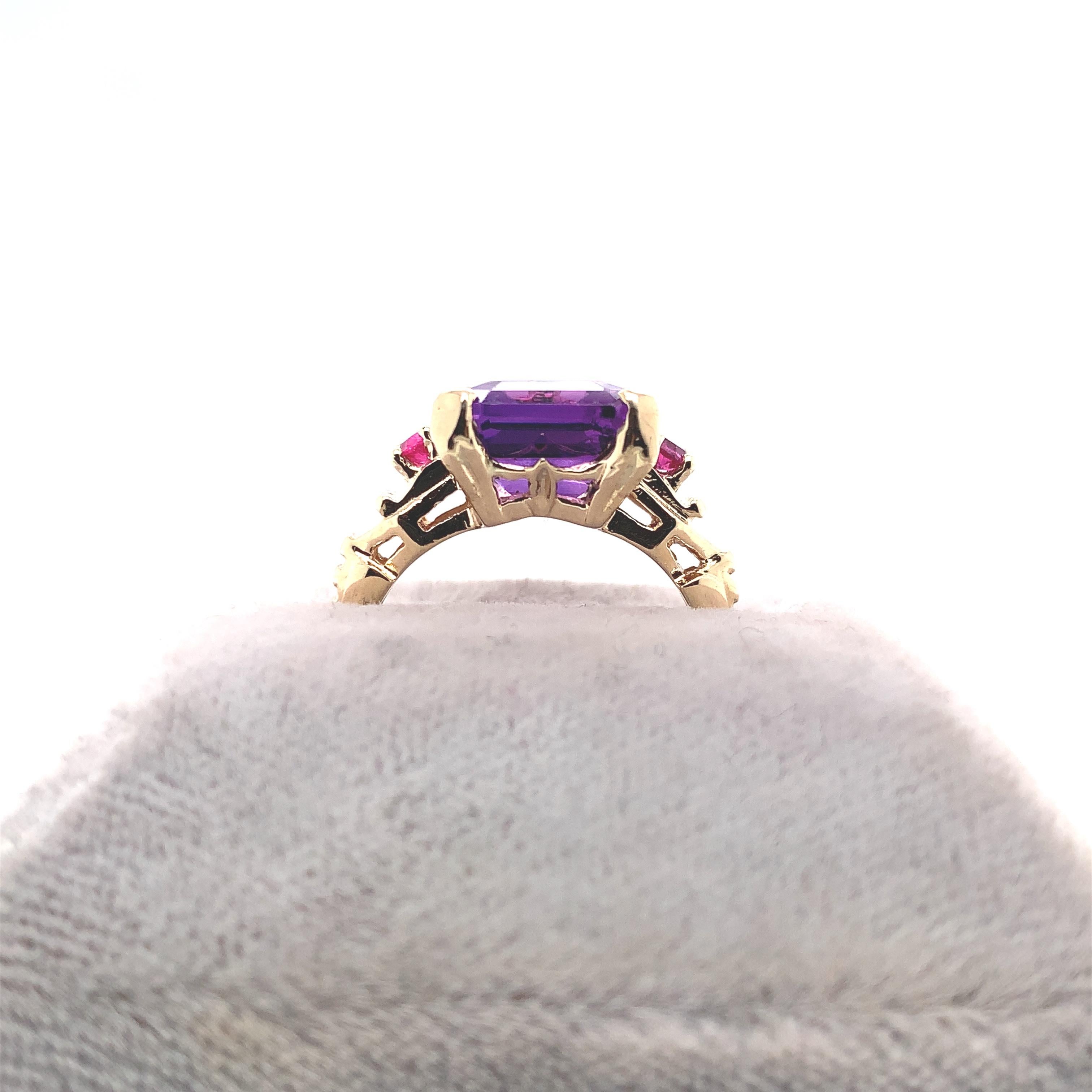 Retro 14K yellow gold amethyst and ruby ring. The ring features an emerald cut medium dark purple amethyst weighing 5.24 carats and measuring about 12mm x 10mm. There is a nick in the stone by one of the prongs. Two round rubies, measuring about