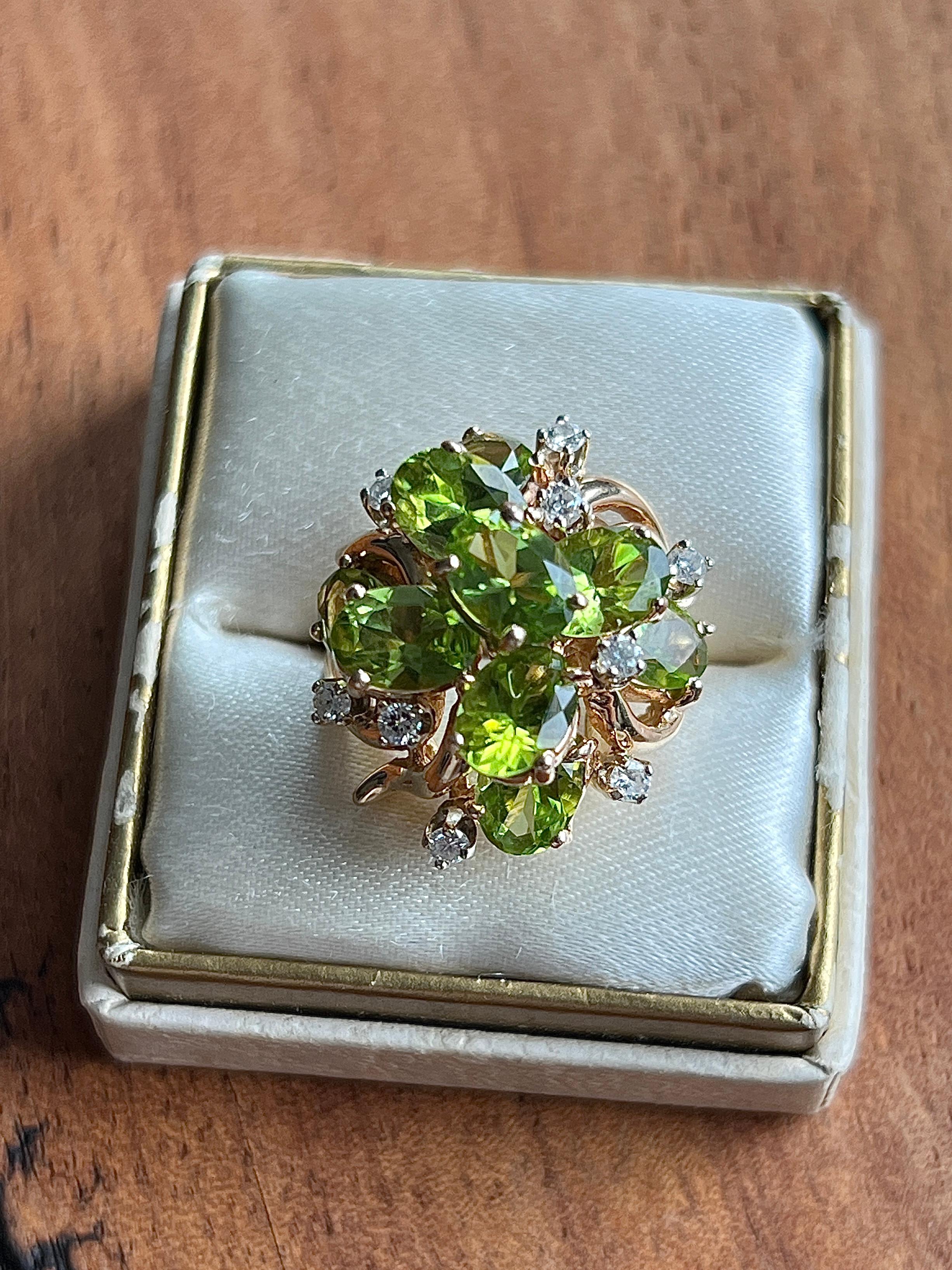 Un anillo de cóctel vintage de los años 70, elaborado en oro amarillo de 14 quilates, con nueve vibrantes gemas ovales de peridoto que miden aproximadamente 7 x 5 mm cada una, con un peso total en quilates de 7,87. Los exuberantes peridotos verdes