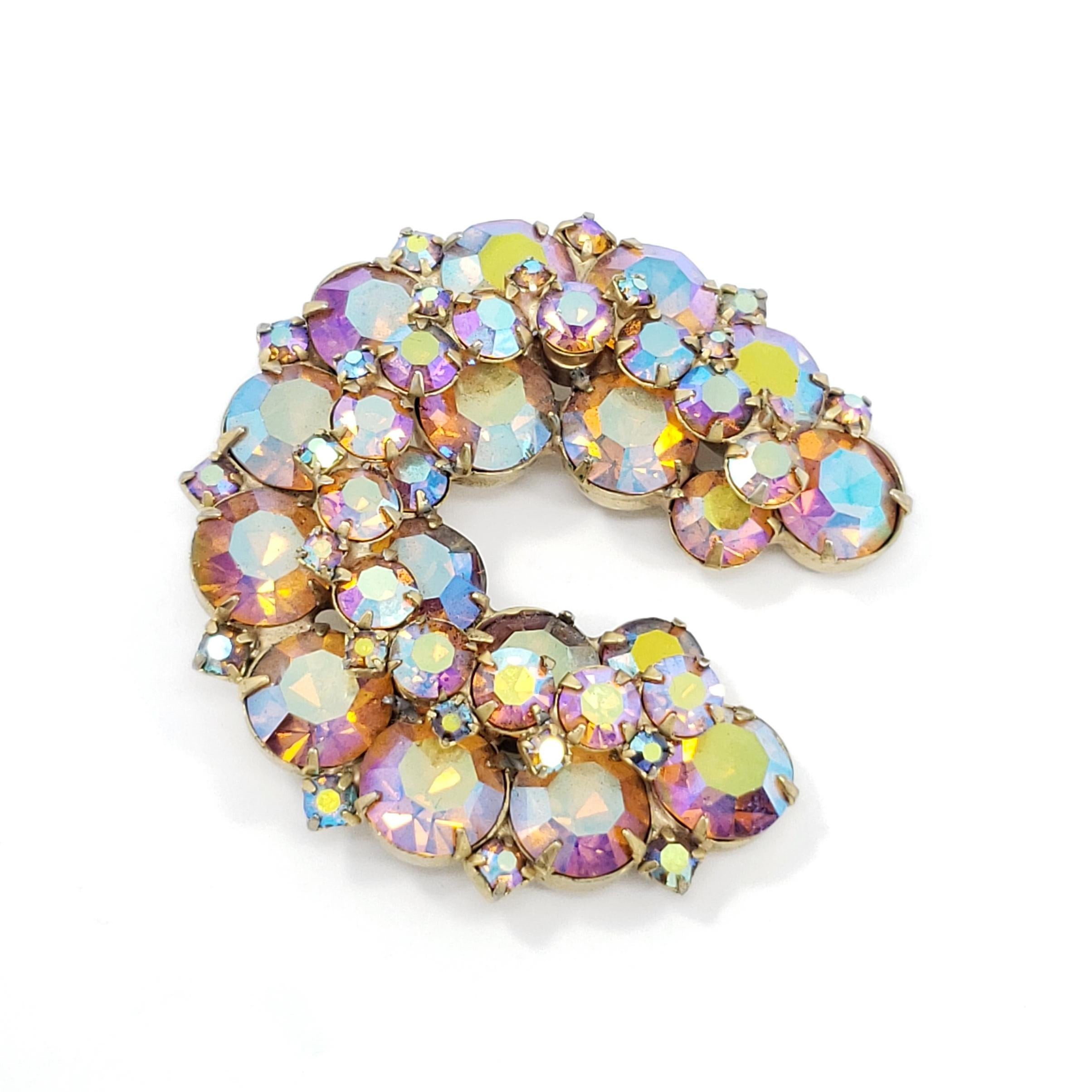 A stylish open round retro brooch. This accessory features sparkling, fuchsia, aurora borealis crystals. Prong-set in a vintage, wreath-shaped, brass-tone setting.
