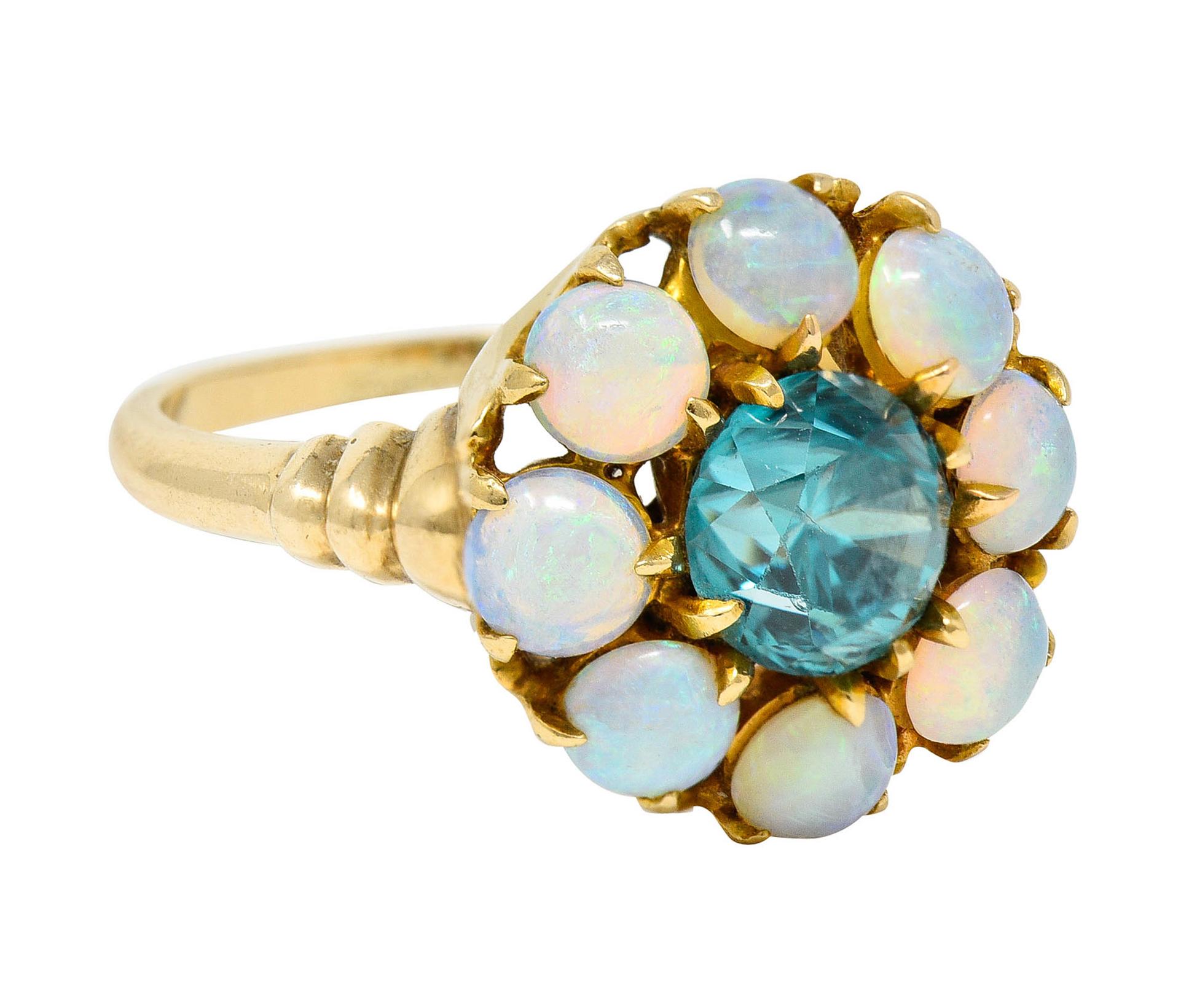 Centering a 6.0 mm round cut zircon with saturated greenish blue color

Surrounded by a halo of 3.5 mm round opal cabochons

Well matched white body color with strong green and yellow play-of-color

Completed by ribbed shoulders

Stamped 14K for 14