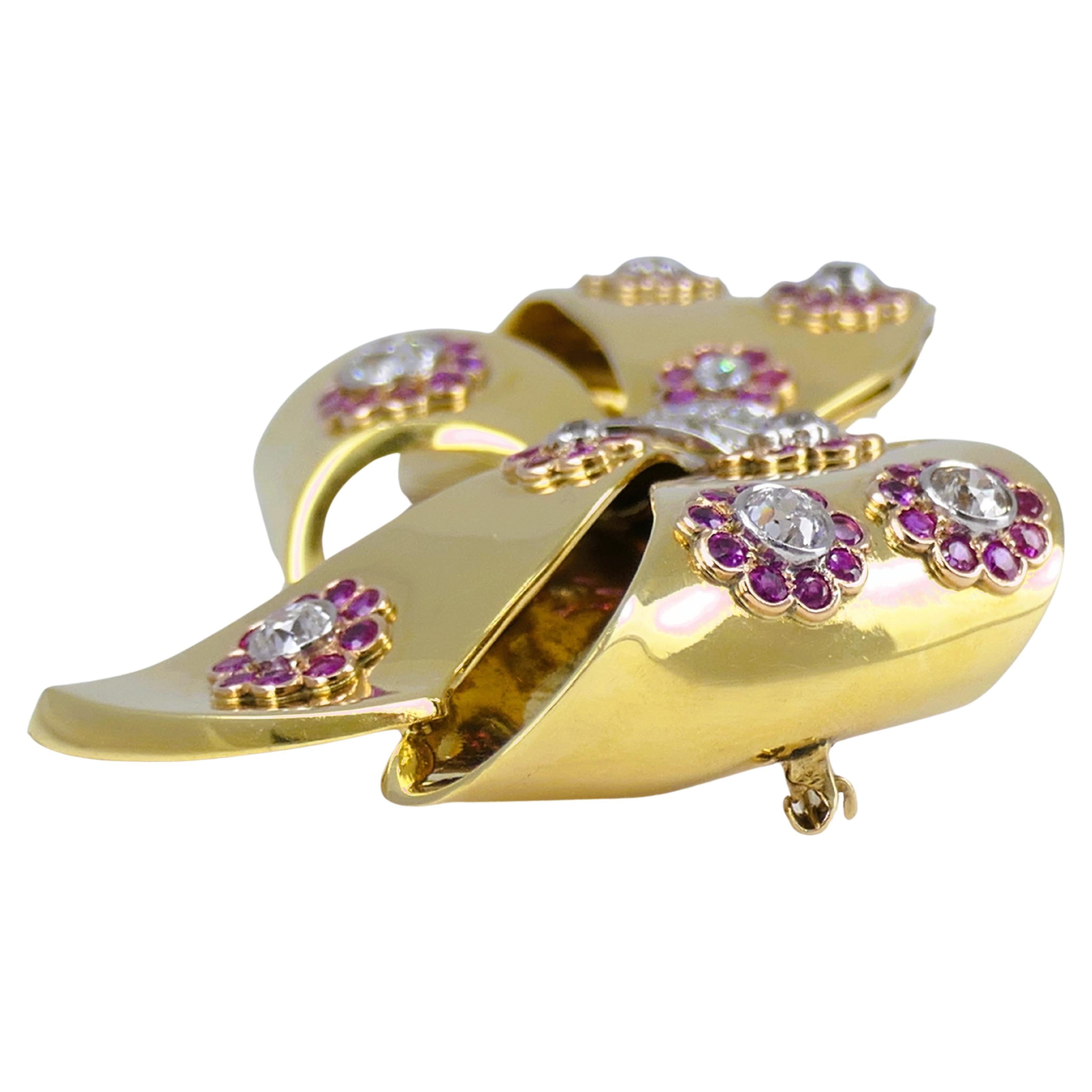 A lovely Retro bow brooch pin made of 18k gold with ruby and diamond.
The gemstones are assembled in beautiful florets, with ruby “petals” and diamond “stamens”. The bow is tied in the center with a white gold ribbon adorned with diamonds. 
This