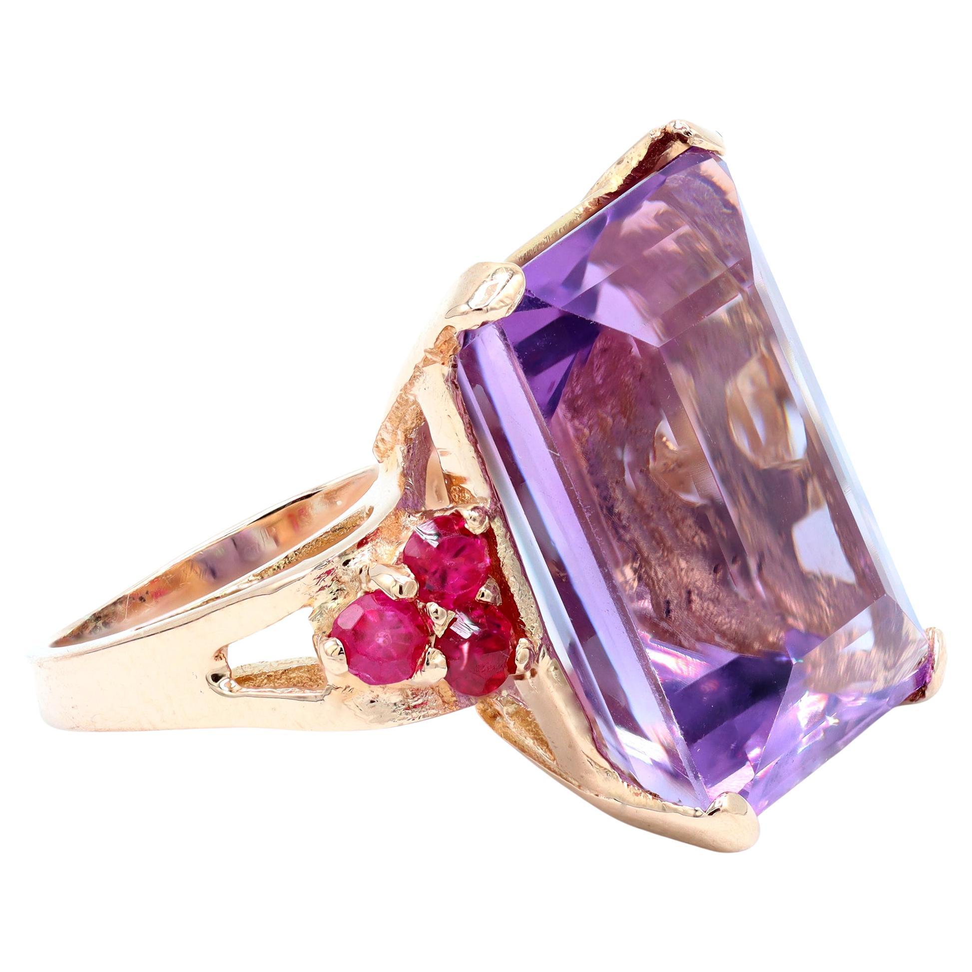 A statement Cocktail ring Circa 1940 featuring a step cut light purple amethyst accented with burma rubies on the shoulders. The retro ring is set in rose gold and has a gross weight of 8.4 grams. The Amethyst weighs approximately 14 carats, the
