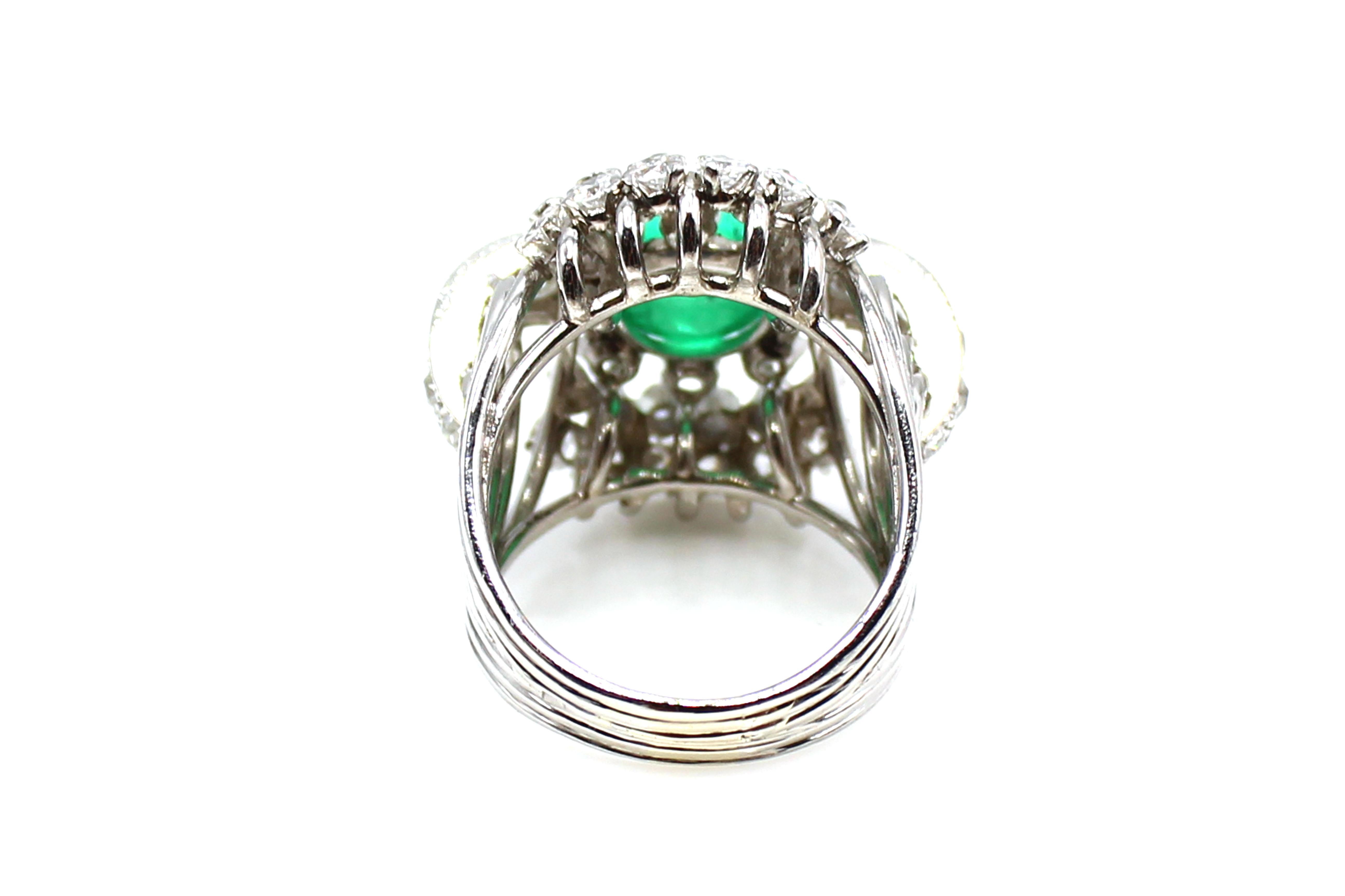 This bold Retro ring from ca. 1950 was wonderfully designed and masterfully hand-crafted in platinum. The center piece of this ring is a deep forest green cabochon emerald measured to weigh approximately 2.5 carats. Surrounding the center gem-stone,