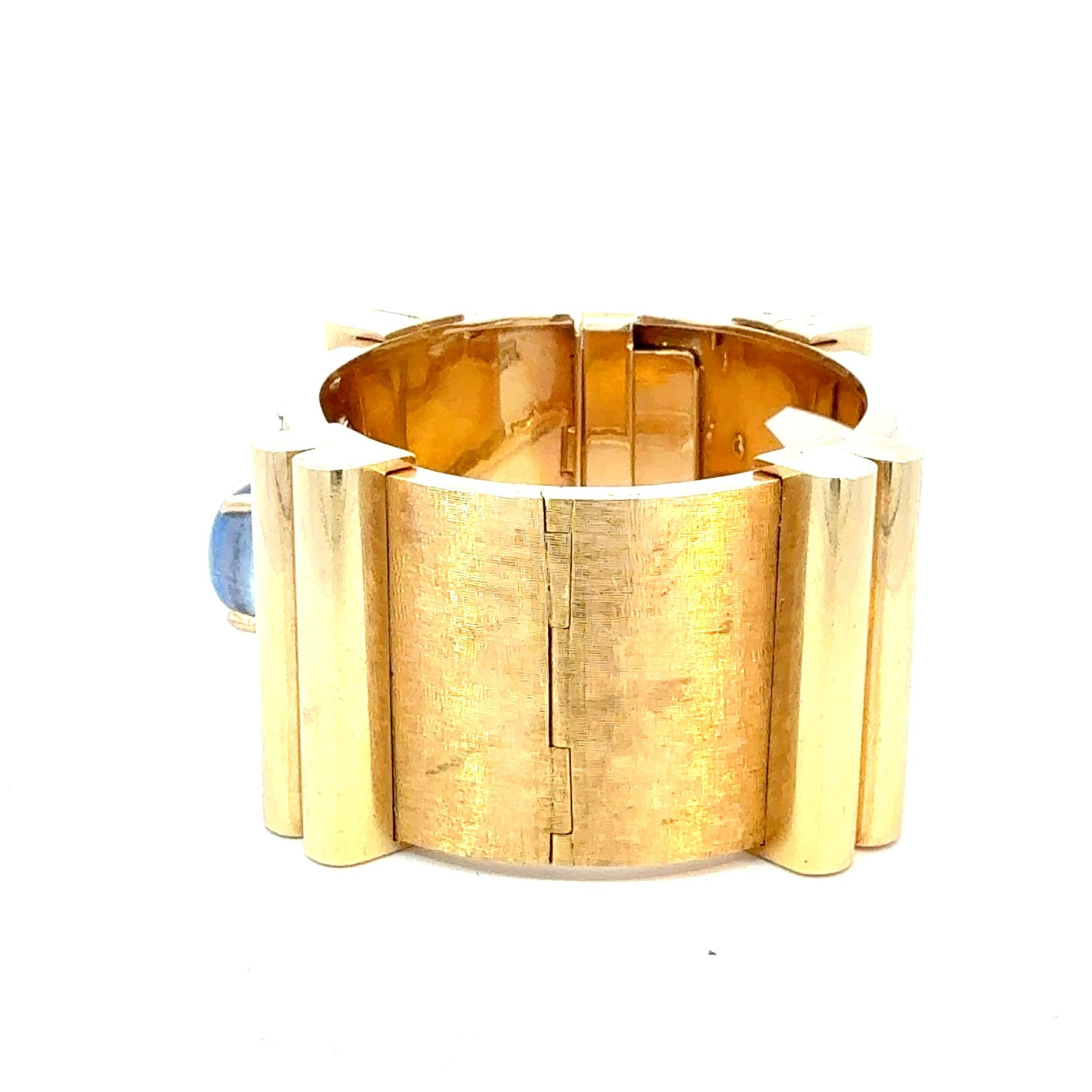Questo splendido braccialetto bangle in oro giallo 14K è caratterizzato da uno zaffiro cabochon al centro, circondato da una costellazione di 17 diamanti taglio brillante del peso di 1,20 carati. Il design fatto a mano presenta una finitura a felce