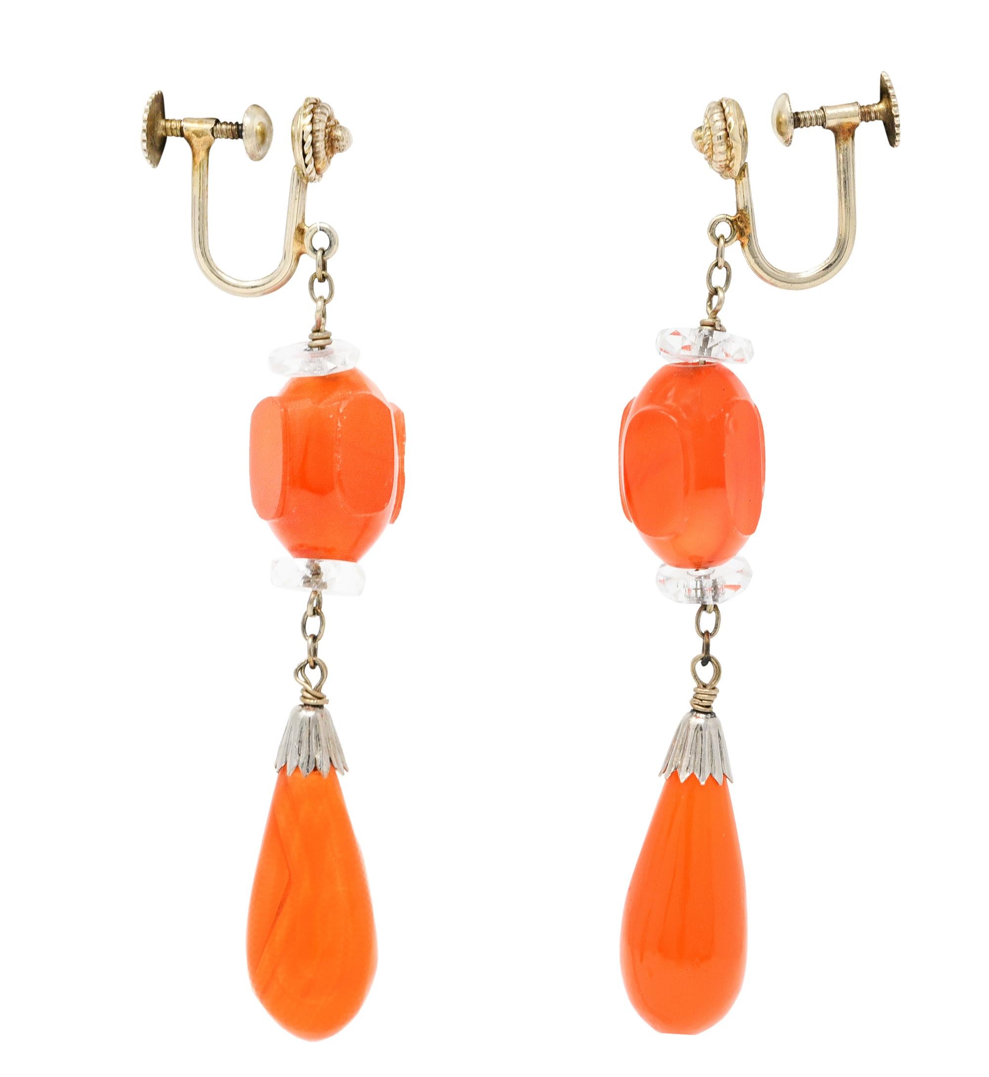Screw back earrings feature uniquely carved carnelian surmounts

Suspending an articulated pampel drop of carved carnelian

Very well matched and a translucent orangey red color

Accented by faceted rock crystal rondelle spacer beads

Completed by a