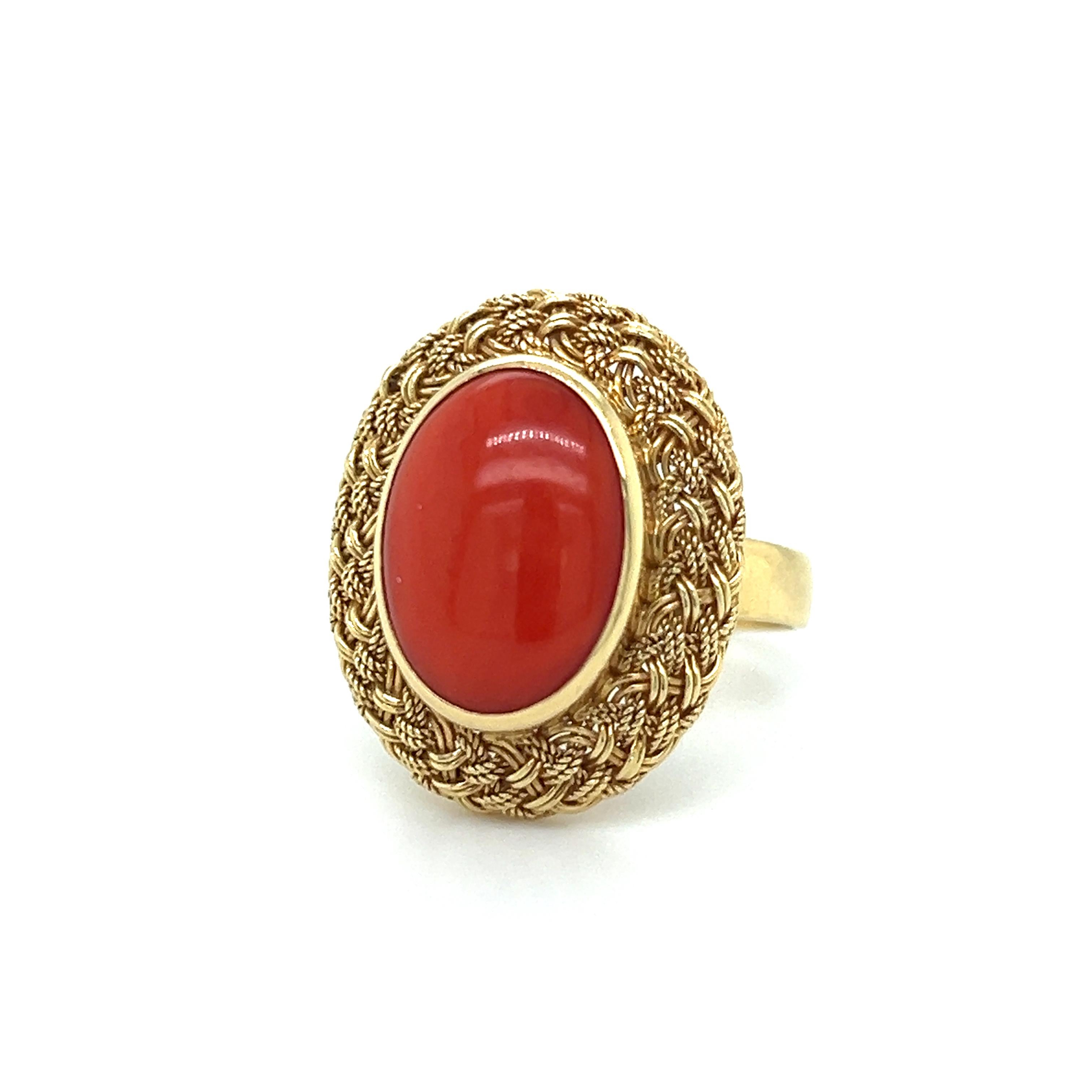 Beautifully made cocktail ring in 18k yellow gold. The ring highlights one cabochon cut coral gemstone. The gemstone is bezel set and encased in a basket weave pattern that highlights the vibrant red colored gem. 
The gemstone measures 13 x 10 mm