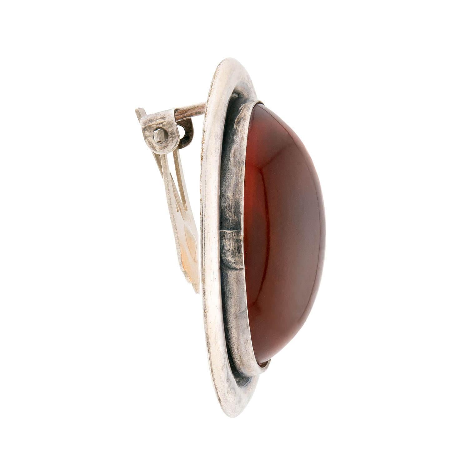 A beautiful pair of amber earrings from the Retro (ca1940s) era! Crafted in sterling silver, each oval-shaped earring features a large amber cabochon. The amber stones are held within a smooth and simple bezel setting, and displays a lovely