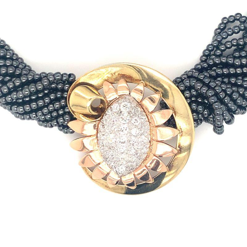 One Retro diamond and hematite bead necklace with a 14K yellow and rose gold circular diamond enhancer featuring 40 old European cut, platinum pave-set diamonds totaling 2 ct. Designed with a platinum navette shaped center and ribbon motif border on