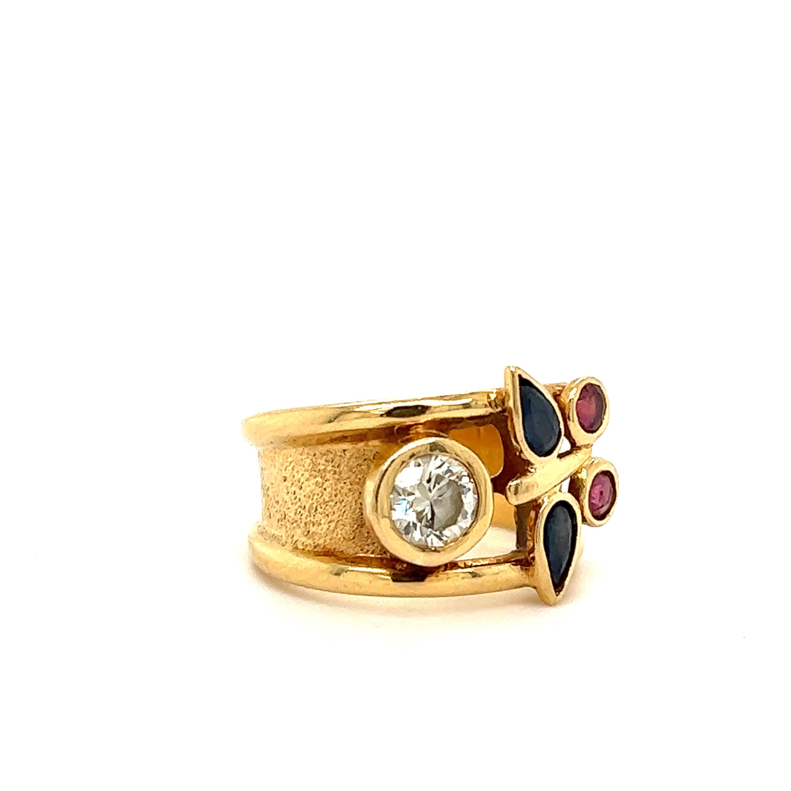 Fantastic design seen on this retro wide band design. The ring is crafted in 18k yellow gold and set with natural earth mined diamonds, rubies and sapphires. The ring is set with one approximate 1.00 ct. round brilliant cut diamond that is bezel