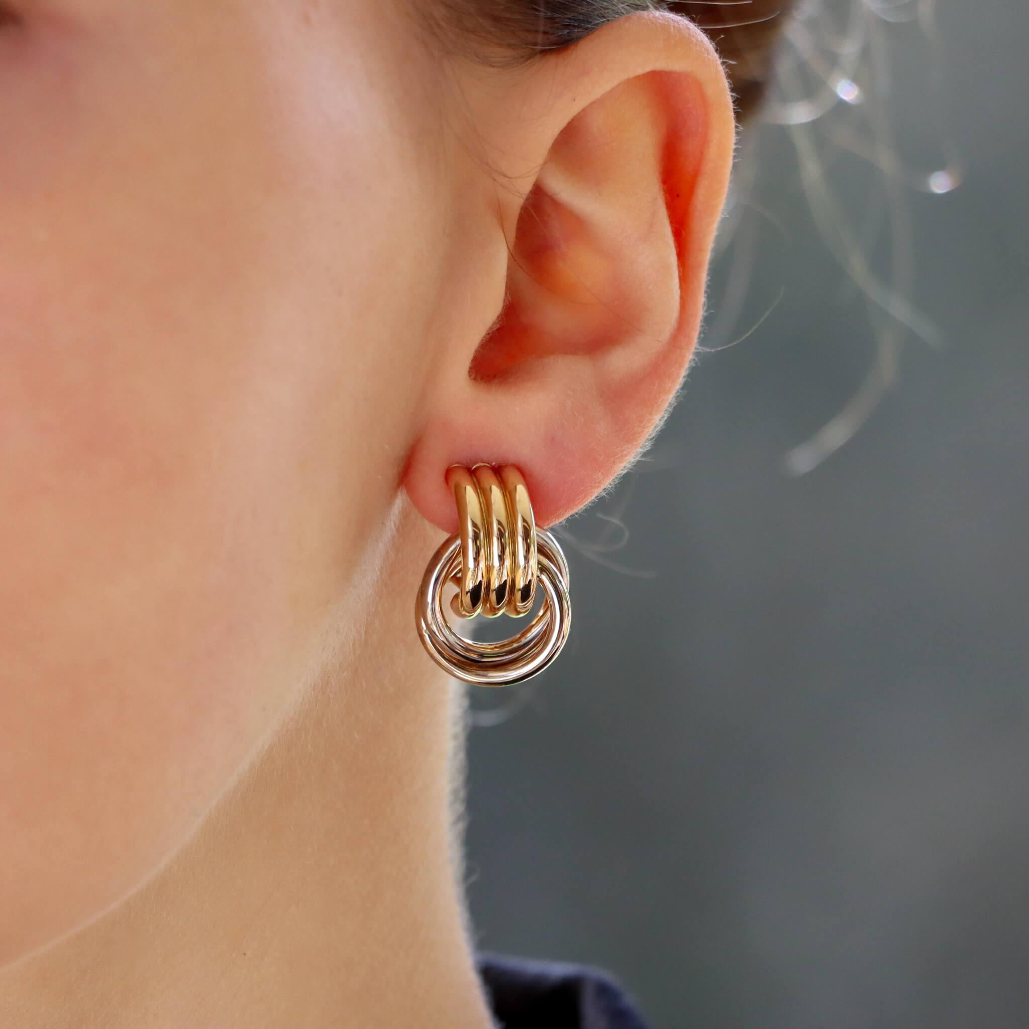 Ein stilvolles, von Türklopfern inspiriertes Paar Ohrringe aus 14k Gelb- und Weißgold.

Jeder Ohrring besteht aus einem ineinandergreifenden, gelöteten Ring, der elegant an einem halben Reif hängt. Der halbe Reif besteht aus drei gelöteten