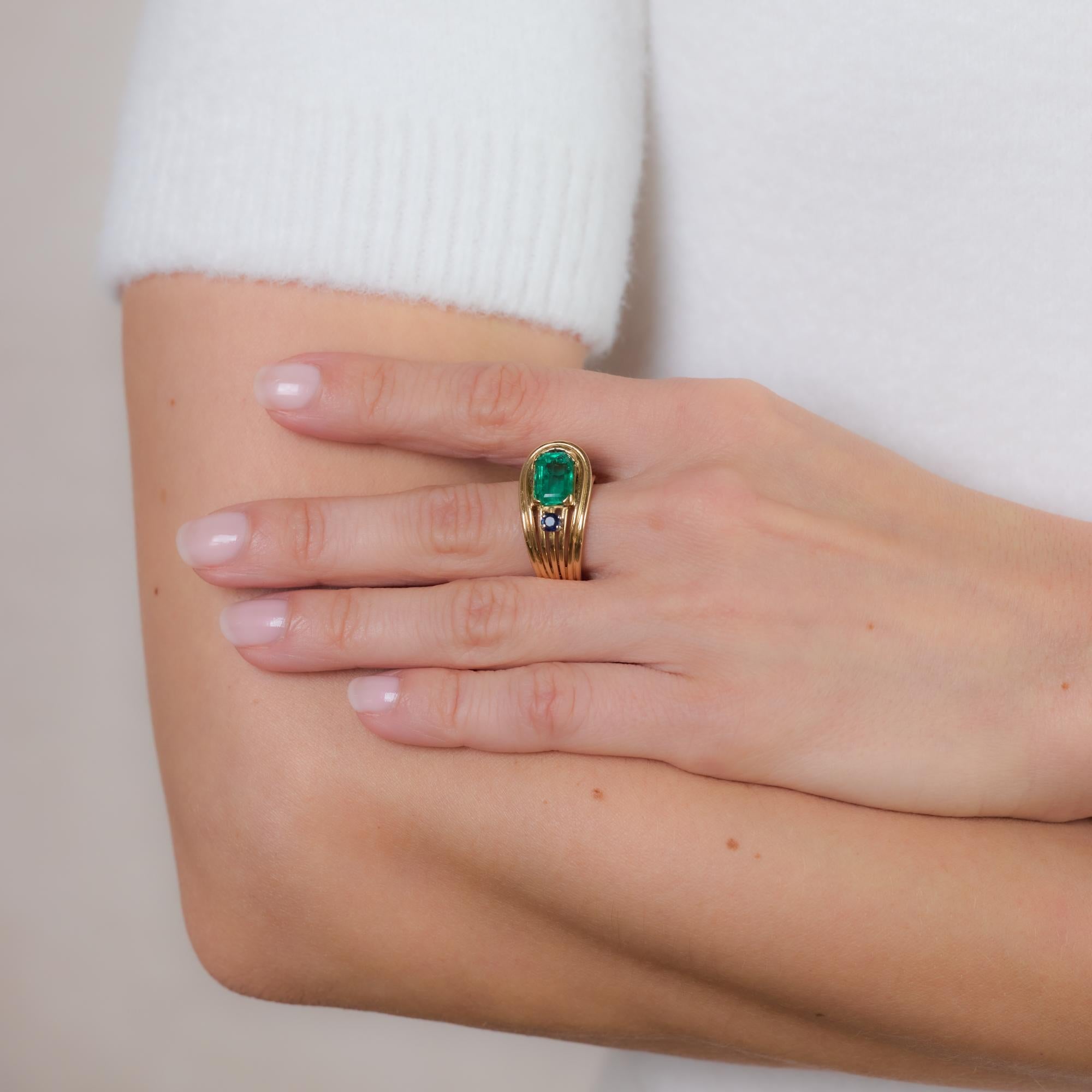 This striking Retro 18k rose gold cocktail ring features a vibrant approximately 2-carat emerald-cut emerald, complemented by a deep blue round brilliant cut sapphire of approximately 0.20 carats. A bold and elegant design with timeless vintage