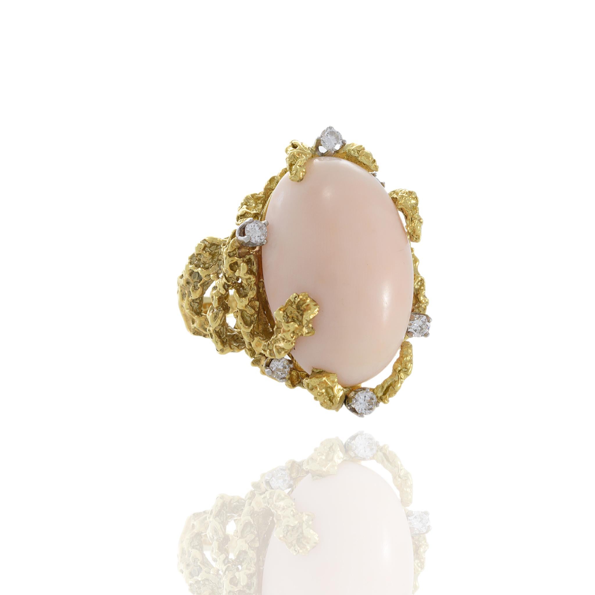 The 18KT Yellow Gold Retro Era Natural Angel Skin Coral and Diamond Cocktail Ring is a testament to the elegance and glamour of vintage jewelry design. This exceptional piece beautifully combines the soft, ethereal beauty of natural angel skin coral