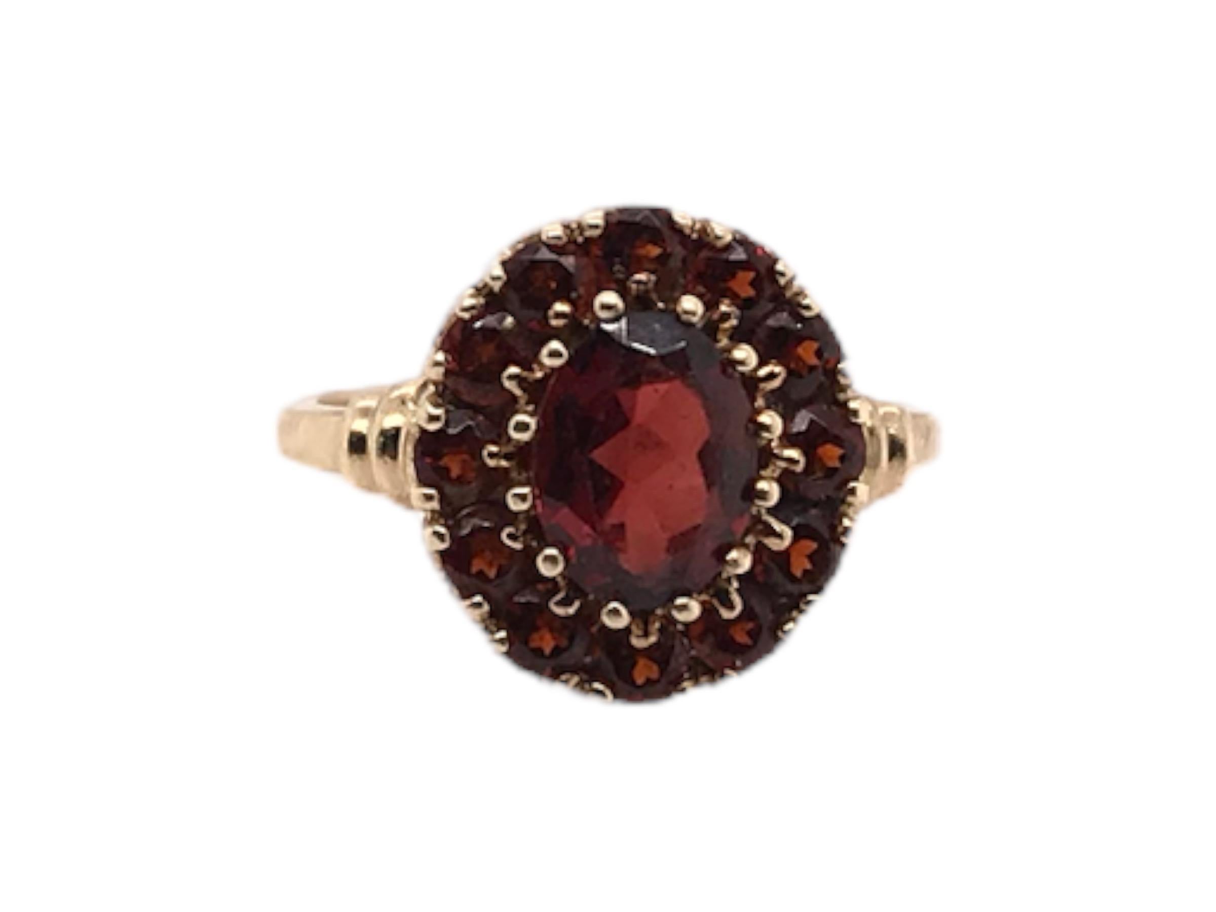 This vintage beauty is from the Retro Era, 1940 - 1960. Made in 10K yellow Gold. She is absolutely perfect for everyday wear! 
The setting features 1 center oval shaped garnet gemstone surrounded by 12 round garnet gemstones. 

Ring Top