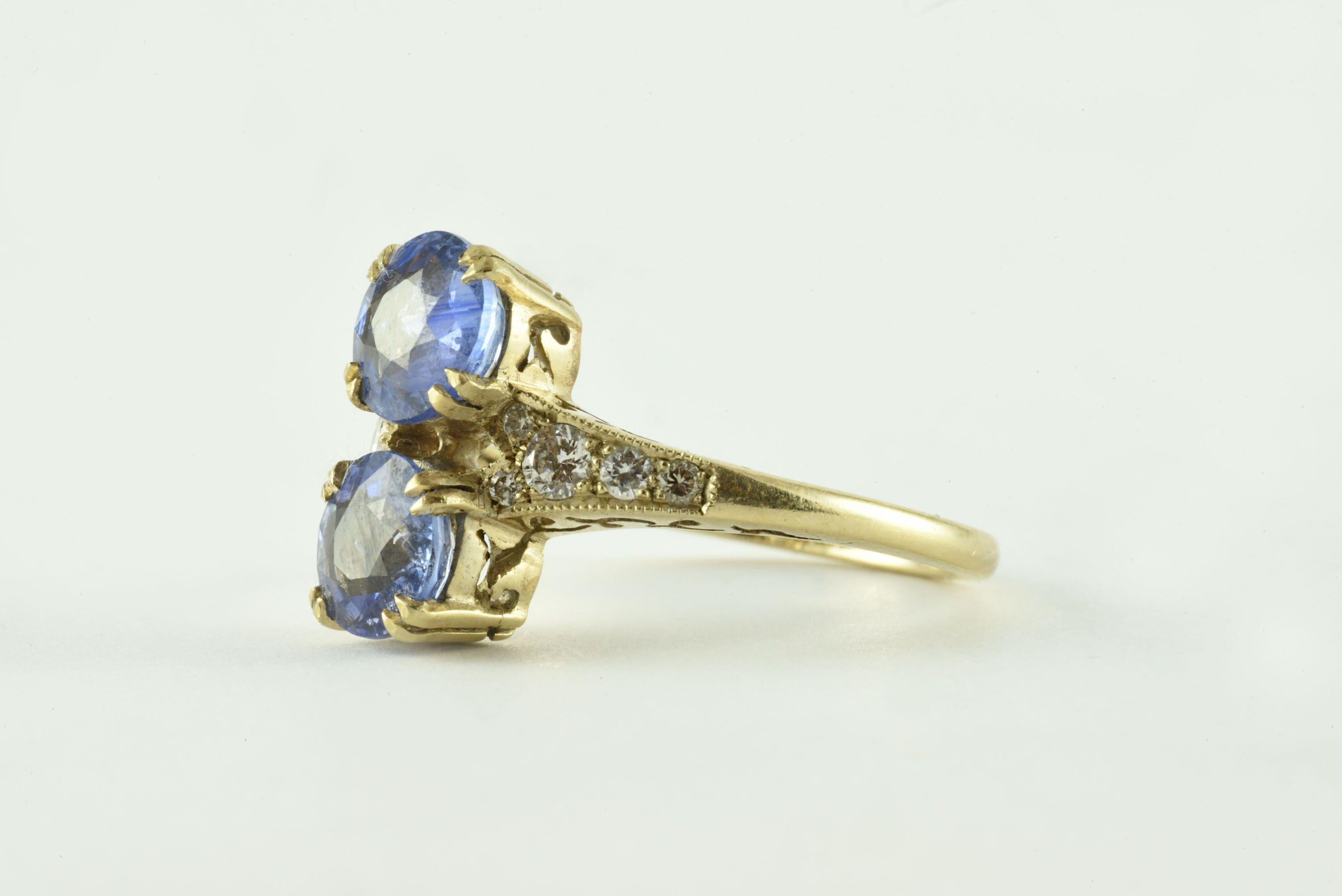 Fabriquée dans les années 1960 en or jaune 18 carats, cette bague vintage est conçue autour de deux saphirs bleus ronds totalisant environ 2,40 carats, avec des épaules ornées de diamants ronds brillants totalisant 0,22 carats, ainsi qu'un délicat