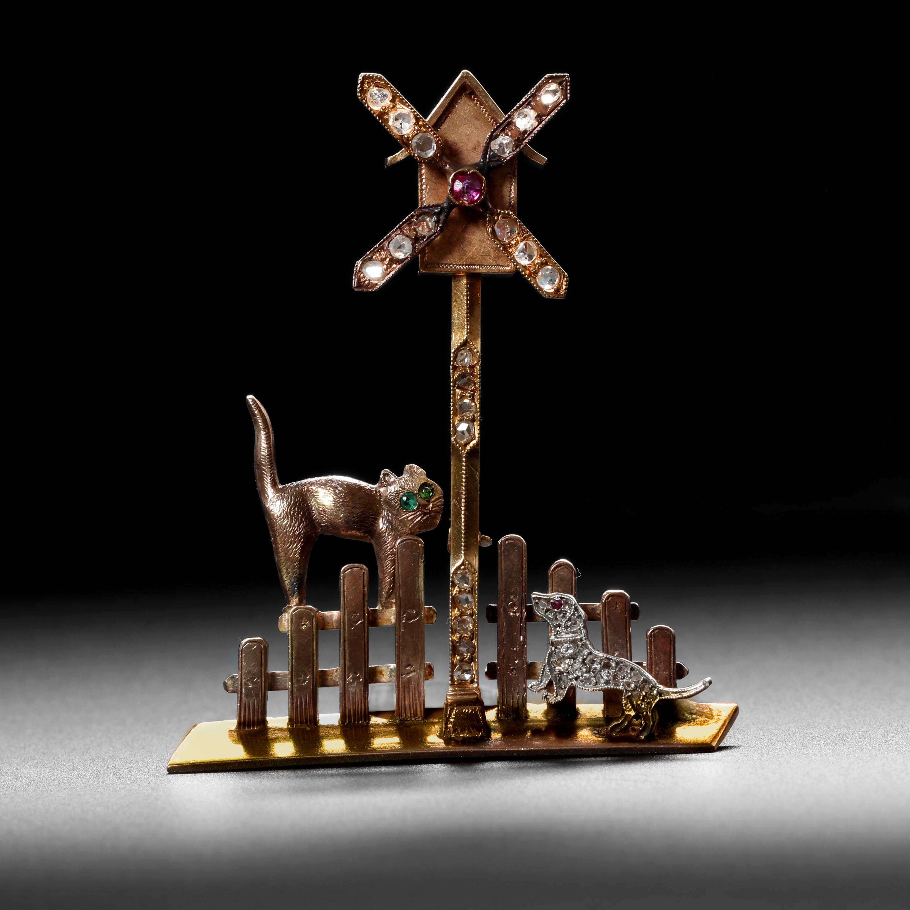 It's not a just a brooch; it's a story; a narrative. 

An emerald-eyed cat and a diamond-encrusted dog with a ruby-red spinel eye both appear quite interested in what would appear to be a cunning bird-house with a windmill attached. The picket fence