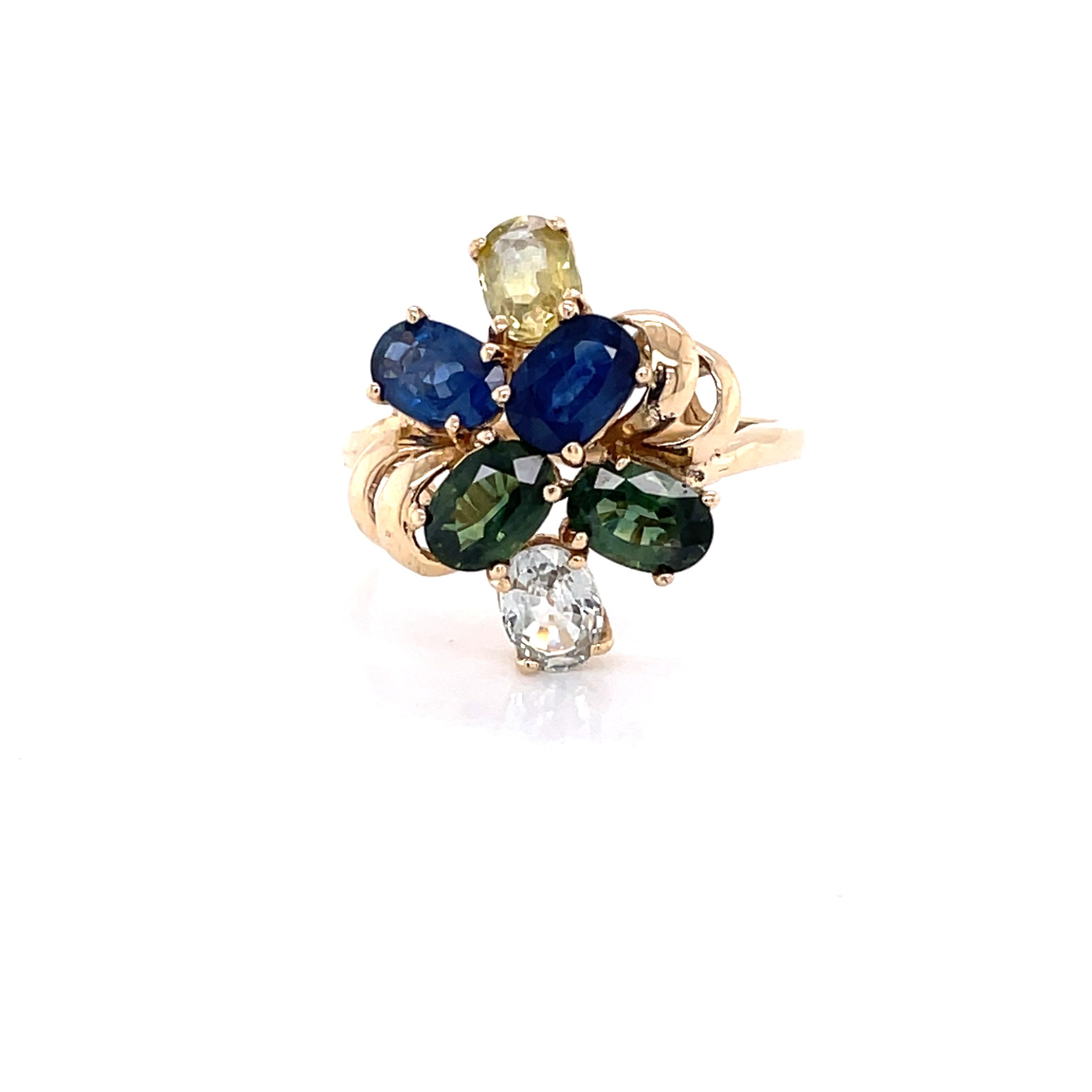 A colorful asymmetrical arrangement of green peridot, blue topaz, blue sapphire, yellow citrine and white zircon creates this pleasing cluster ring, circa 1950. Crafted in 14 karat yellow gold with a raised gallery, the head of this cheerful ring,
