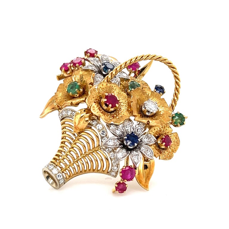 Beautiful design crafted in 18k yellow gold. The brooch depicts a floral bouquet with detail seen throughout. The brooch is set with round diamonds, emeralds, sapphires and rubies. The gemstones are set in a beautiful pattern allowing the brooch to