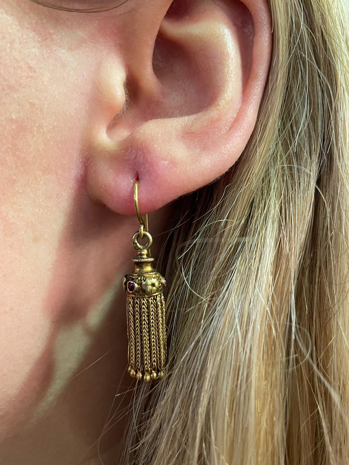 A pair of retro fringed earrings with garnets set in 18 karat yellow gold, circa 1950.

The tops of these fun and playful earrings depict engraved flowers alternating with bezel set cabochon garnets suspending meticulously crafted gold fringes, each