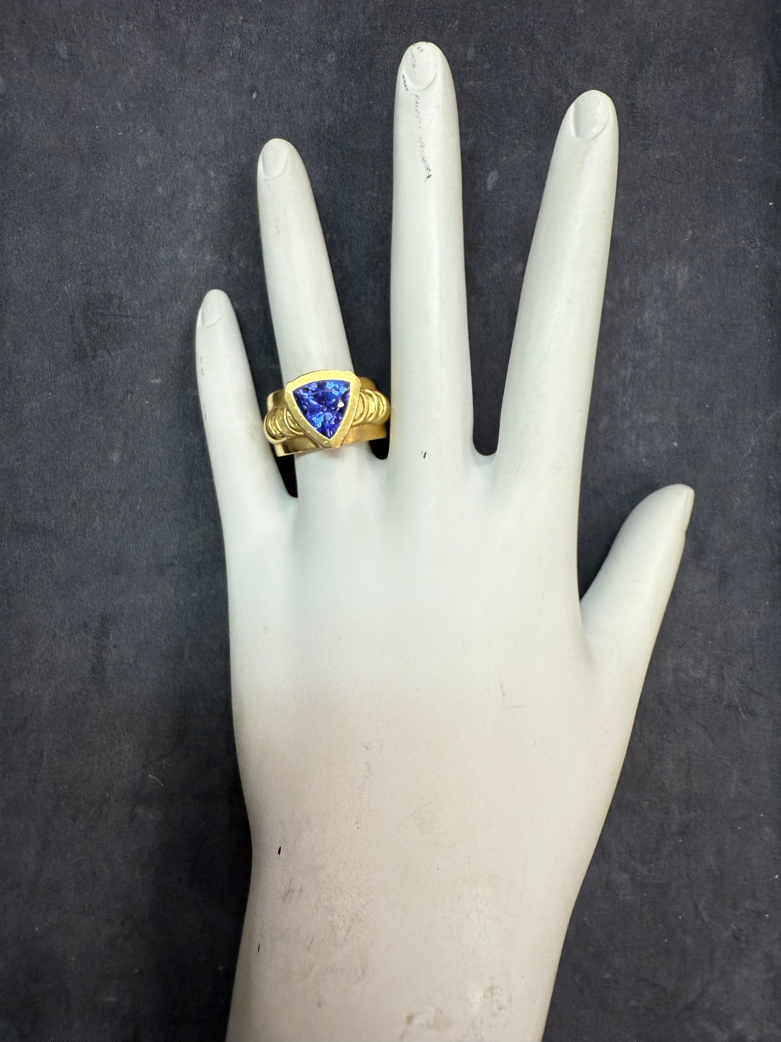 Retro 18K yellow gold ring featuring a trillion-shaped, purplish-blue natural Tanzanite weighing approximately 2.15 carats, measuring about 9 x 9 x 5.7 mm. 
The setting is accented with six natural princess cut colorless diamonds totaling