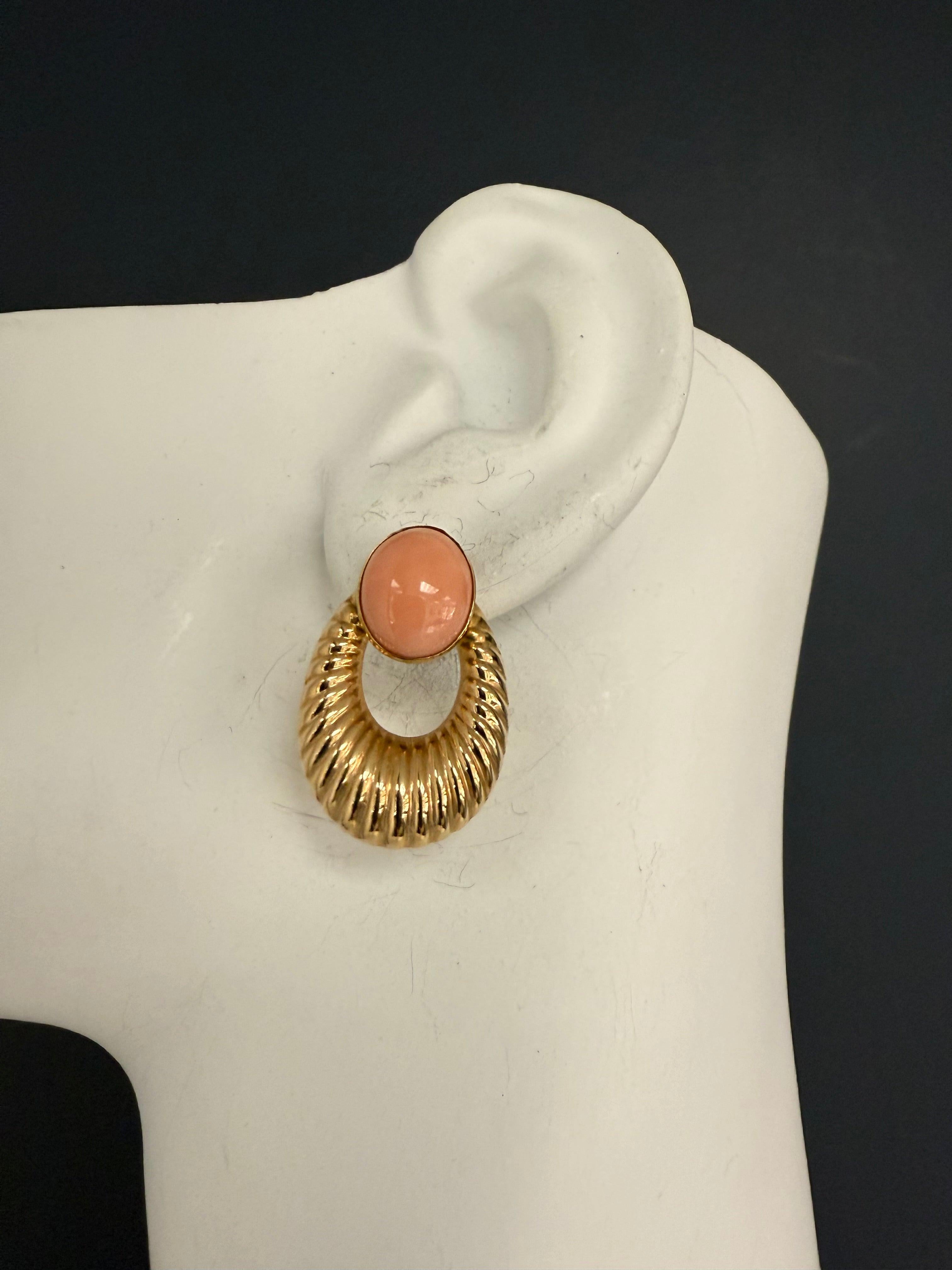 A magnificent pair of retro pink coral cabochon earrings, set in 14K yellow gold and stamped accordingly. Each coral measures approximately 12 x 9.5 mm, showcasing the soft elegance of natural pink coral. The earrings measure approximately 1.25 x