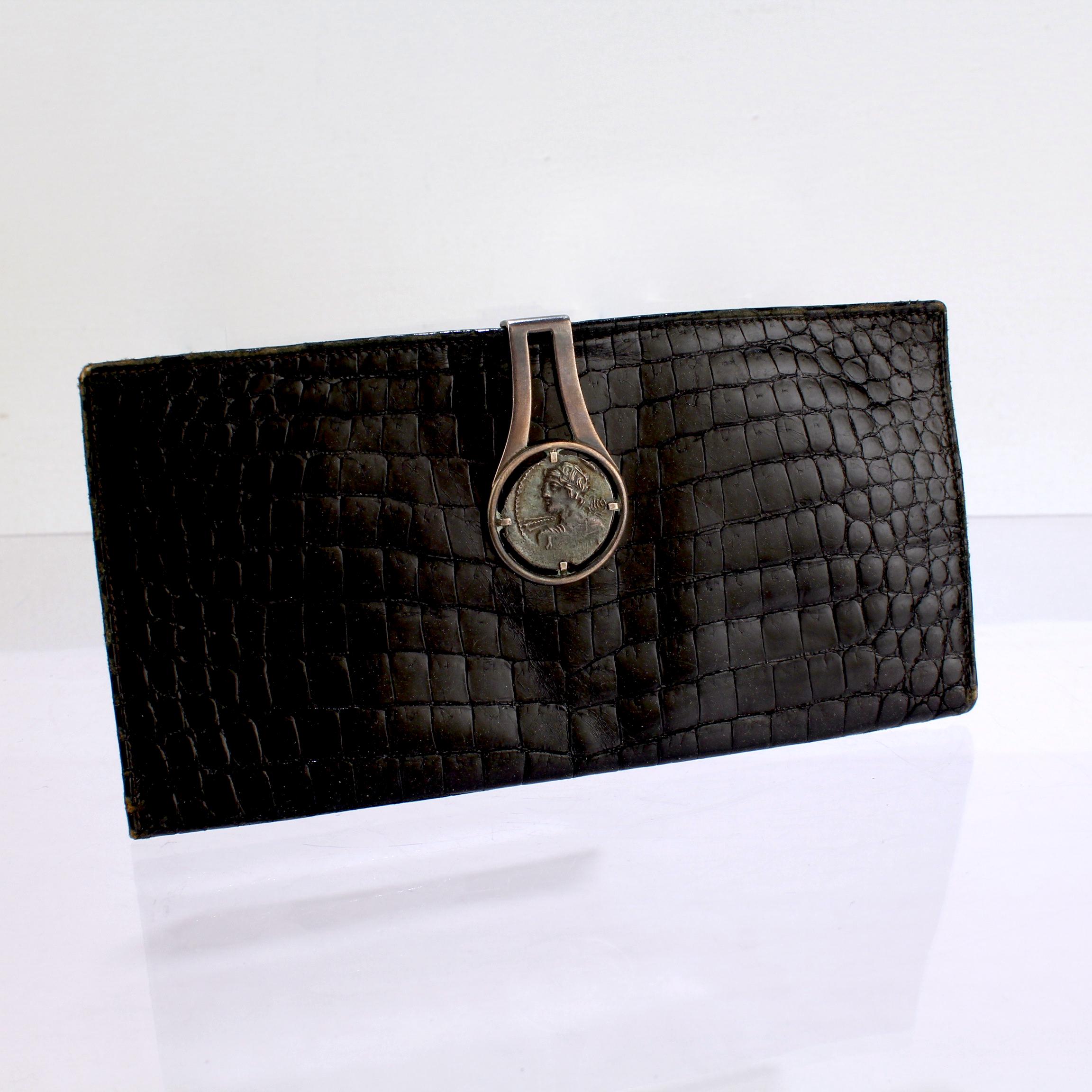 A fine Gucci wallet.

With black faux alligator leather and an integral sterling silver clasp.

The silver clasp is prong set with an silver Ancient Roman style coin.

Simply an amazing wallet from a great retailer! 

Date:
20th Century

Overall