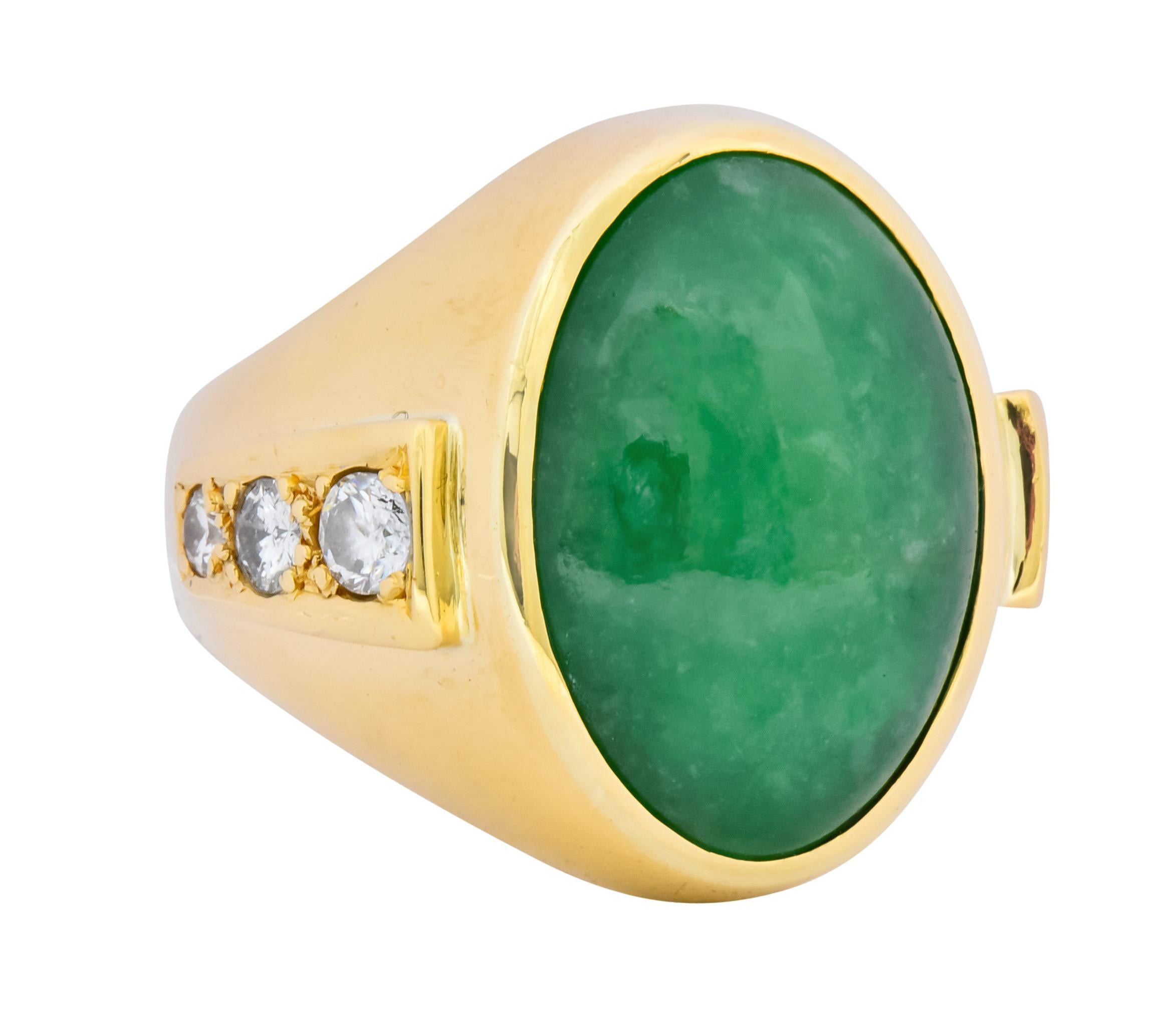 Centering a jadeite jade oval cabochon measuring approximately 20.0 mm x 14.5 mm, translucent and vibrant green in color with subtle mottling

Bezel set in a polished gold surround

Flanked by bead set round brilliant cut diamonds weighing