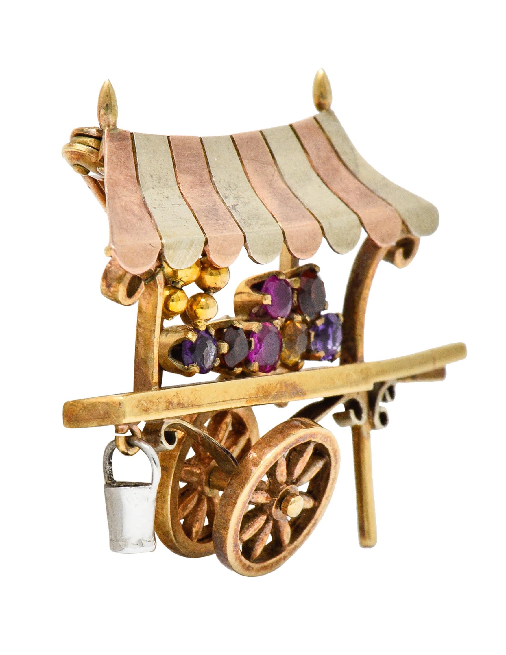Brooch is designed as a vintage flower cart with a striped awning; rose and white gold

Interactive with an articulated white gold bucket charm and rotating wheels

Accented by colorful gemstone flowers - pink sapphire, garnet, amethyst, and