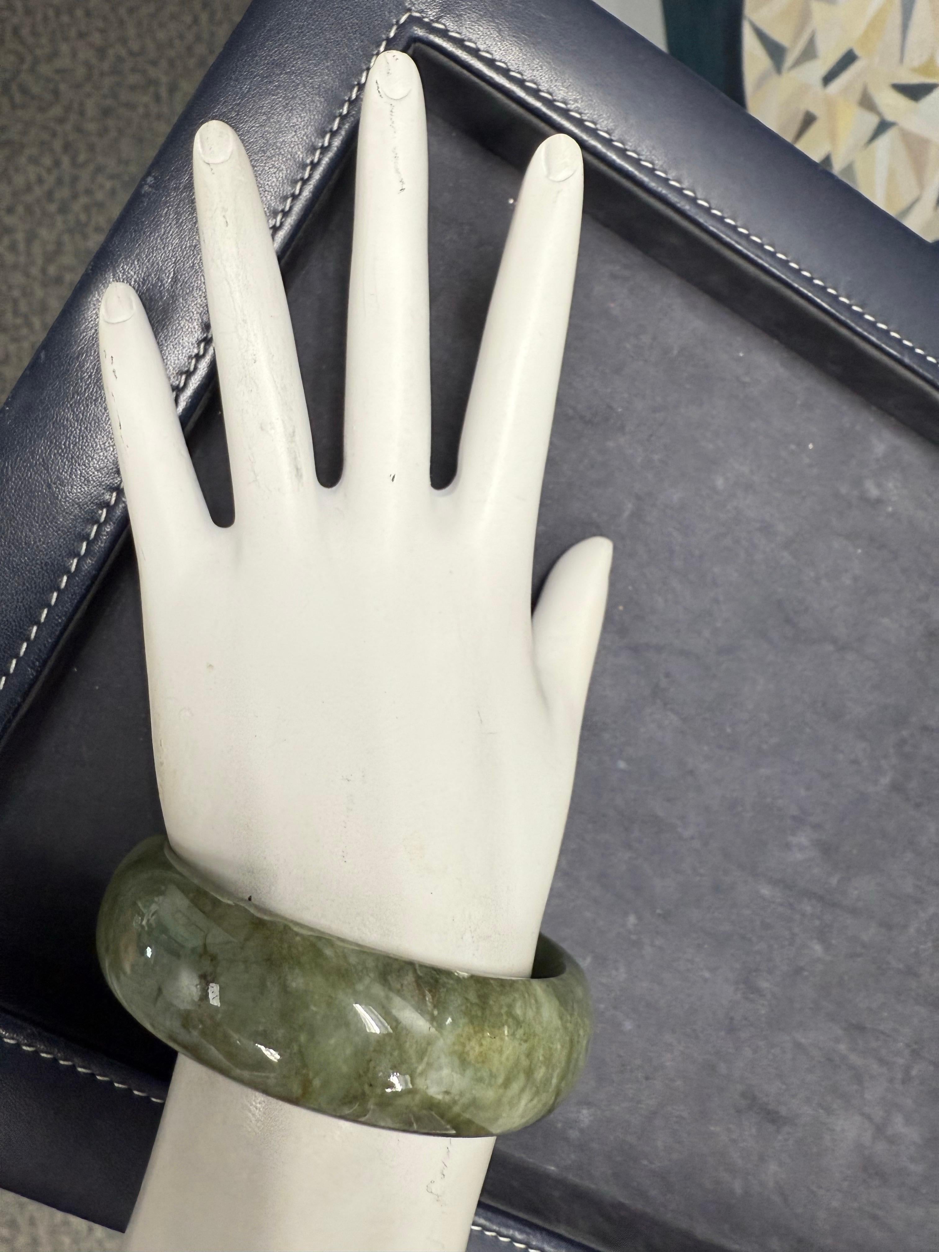 Eleganter Armreif aus grüner Naturjade mit einer Breite von 18 mm und einer Dicke von 7,5 mm, mit einem Innendurchmesser von ca. 6,75 Zoll. Das Armband hat eine glatte, polierte Oberfläche und ist mit einem Gesamtgewicht von 76,8 Gramm sehr präsent.