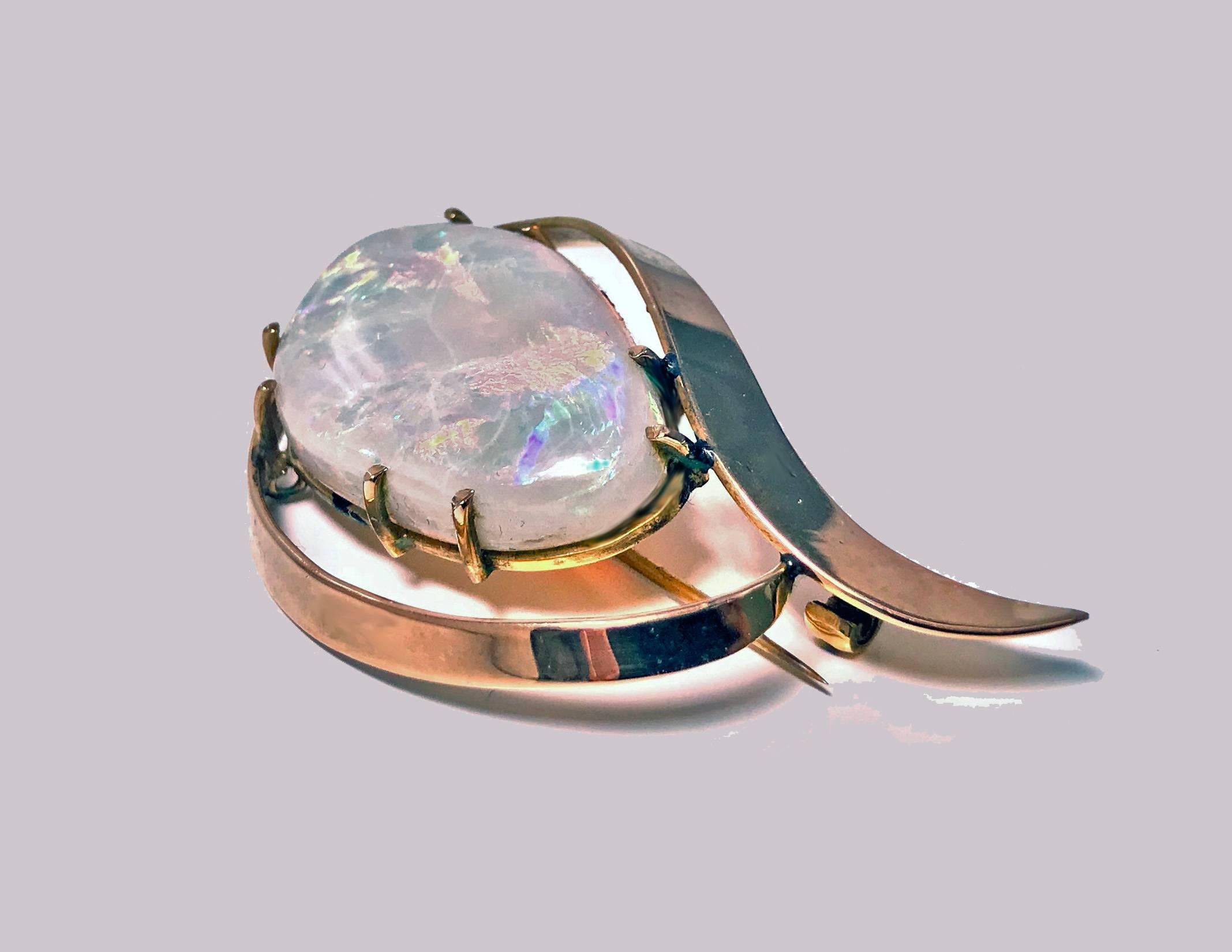 Retro 1960’s large Opal Gold Brooch. The Australian asymmetrical crystal opal gauging approximately 31 x 19 x 5.50 mm semi-translucent good play of colour bright green blue, purple and orange. The opal is claw set with swirl plain polished gold
